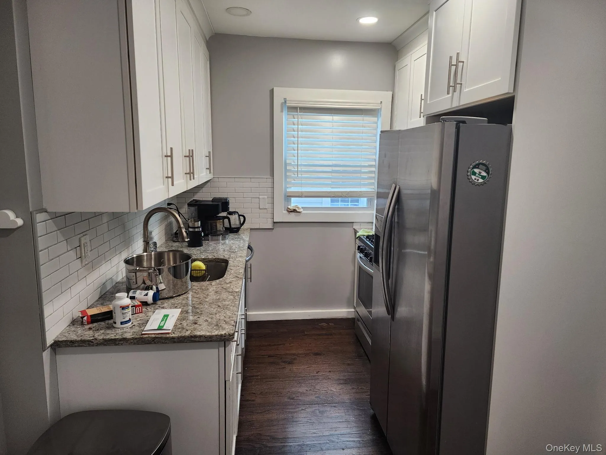 Kitchen featuring white cabinets, light granite counters, stainless steel appliances, decorative backsplash, and dark wood finished floors Kitchen featuring white cabinets, light granite counters, stainless steel appliances, decorative backsplash, and dark wood finished floors