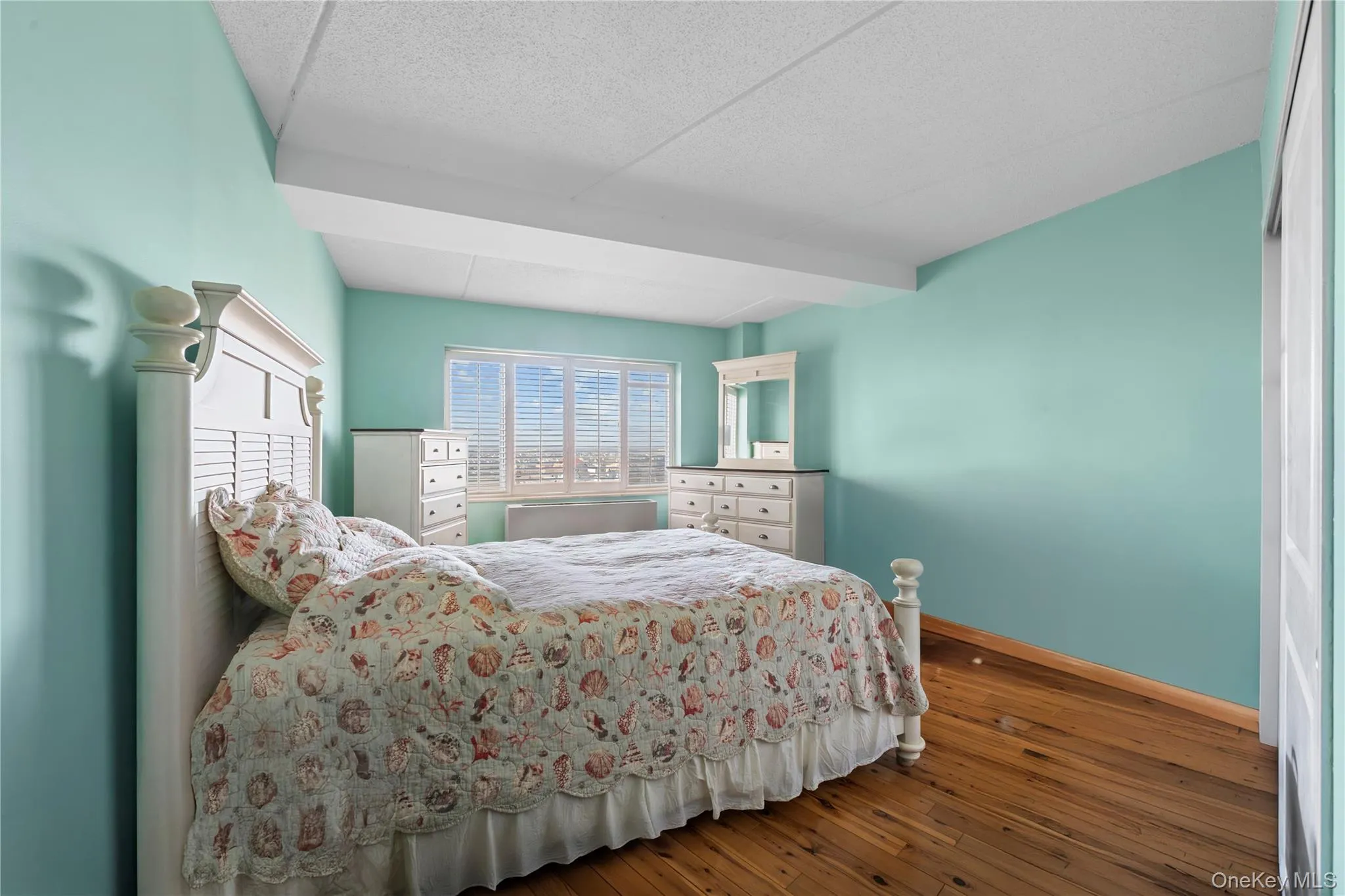 Spacious room featuring wood-finish flooring, light blue wall paint, a broad window with horizontal blinds, and a built-in sliding panel closet Spacious room featuring wood-finish flooring, light blue wall paint, a broad window with horizontal blinds, and a built-in sliding panel closet