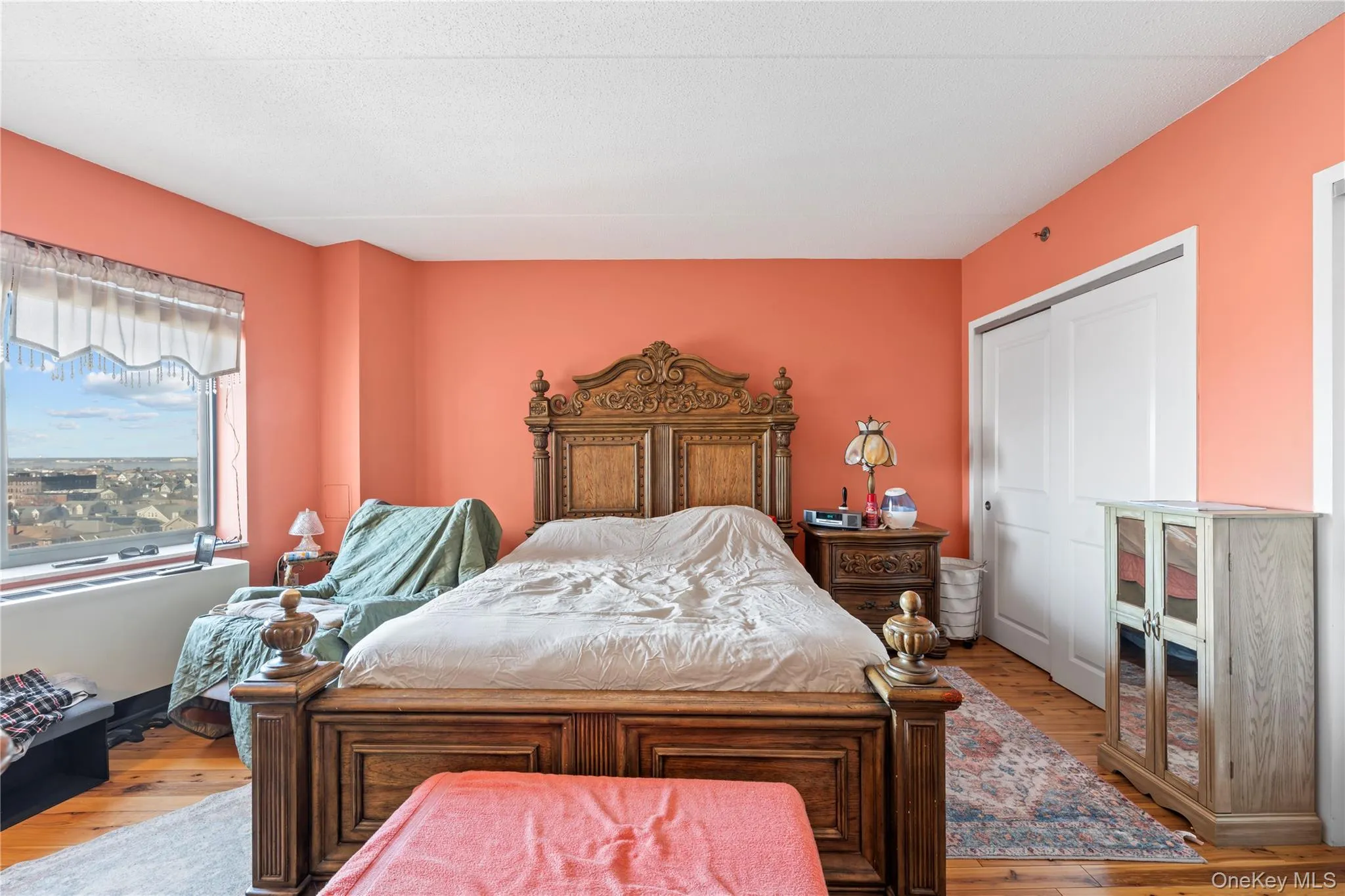 Spacious room featuring wood-finish flooring, a large window offering expansive city vistas, and a closet with white bi-fold doors Spacious room featuring wood-finish flooring, a large window offering expansive city vistas, and a closet with white bi-fold doors