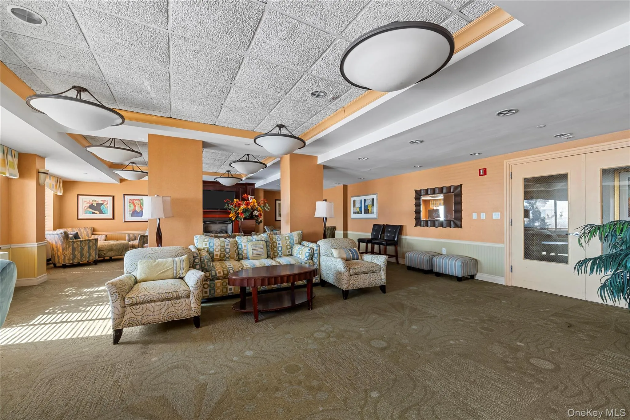Spacious common area featuring patterned carpet flooring, recessed and flush-mount lighting, decorative wall paneling, and a dual-pane glass door Spacious common area featuring patterned carpet flooring, recessed and flush-mount lighting, decorative wall paneling, and a dual-pane glass door
