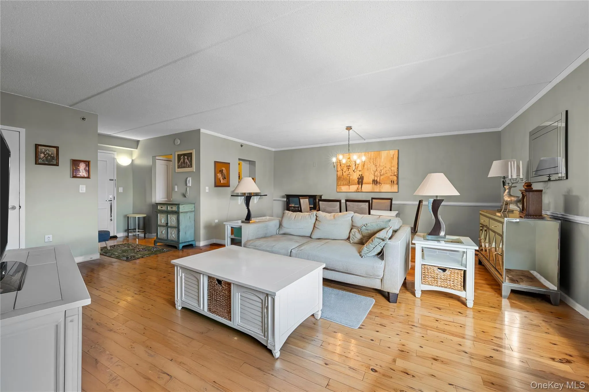 Expansive living area featuring wood-finish flooring, light gray wall tones, and white crown molding Expansive living area featuring wood-finish flooring, light gray wall tones, and white crown molding