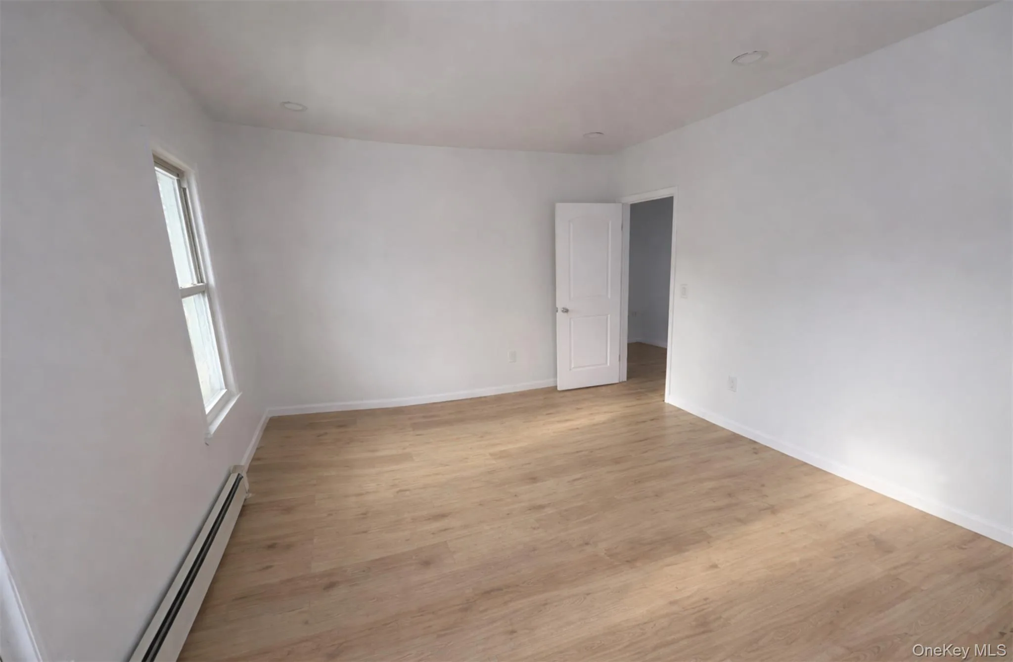 Empty room with baseboard heating and light wood finished floors Empty room with baseboard heating and light wood finished floors