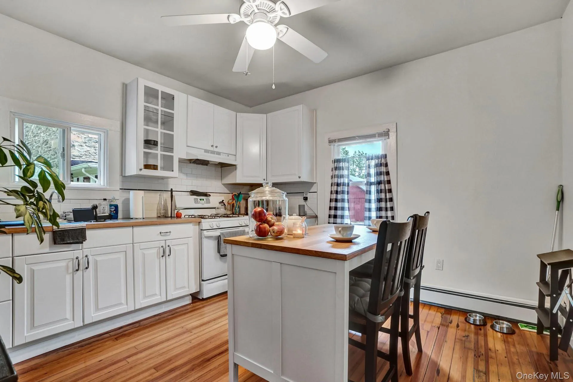 Kitchen featuring backsplash, white gas stove, wood counters, baseboard heating, and white cabinetry Kitchen featuring backsplash, white gas stove, wood counters, baseboard heating, and white cabinetry