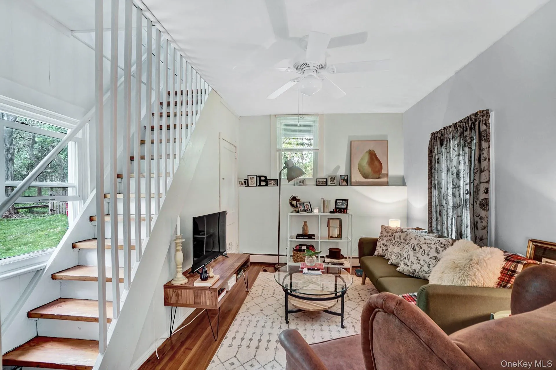 Living area with stairway, a baseboard heating unit, a ceiling fan, and wood finished floors Living area with stairway, a baseboard heating unit, a ceiling fan, and wood finished floors