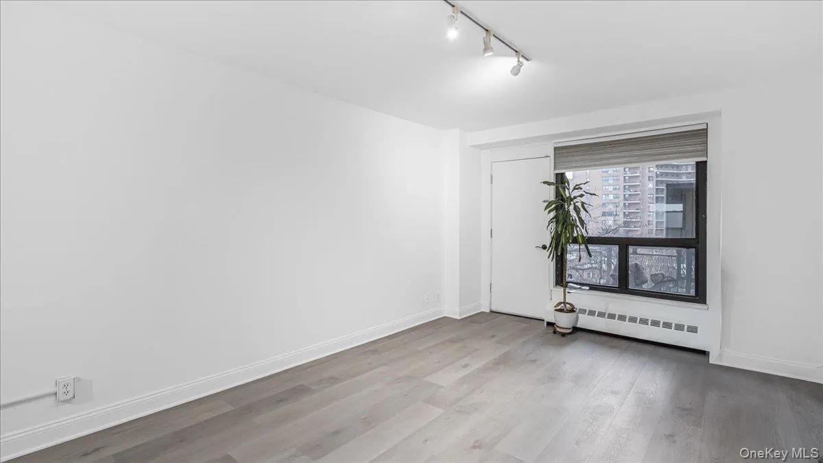 Empty room with light wood finished floors, baseboard heating, and rail lighting Empty room with light wood finished floors, baseboard heating, and rail lighting