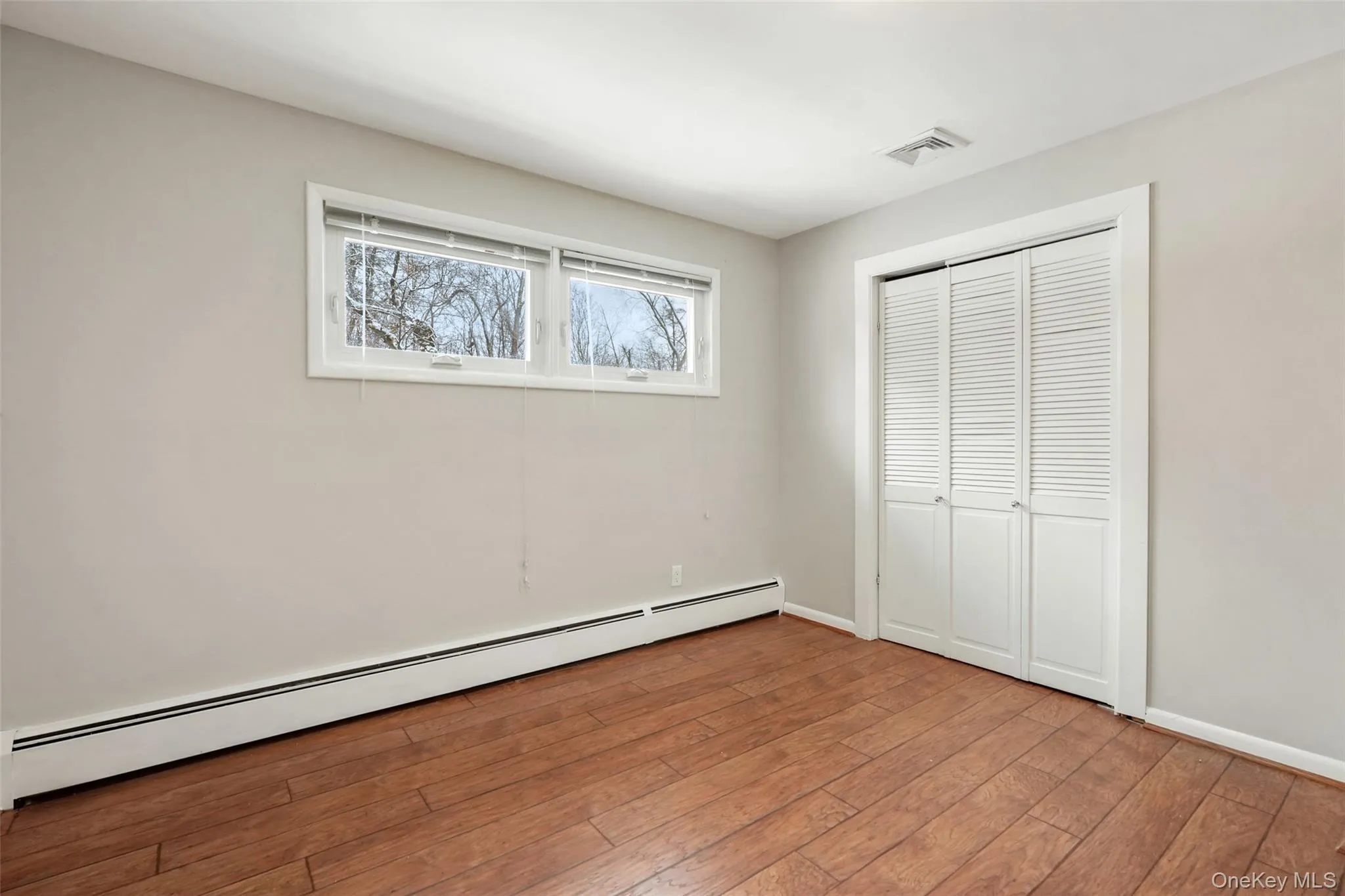 Unfurnished bedroom with baseboard heating, hardwood / wood-style flooring, and a closet Unfurnished bedroom with baseboard heating, hardwood / wood-style flooring, and a closet