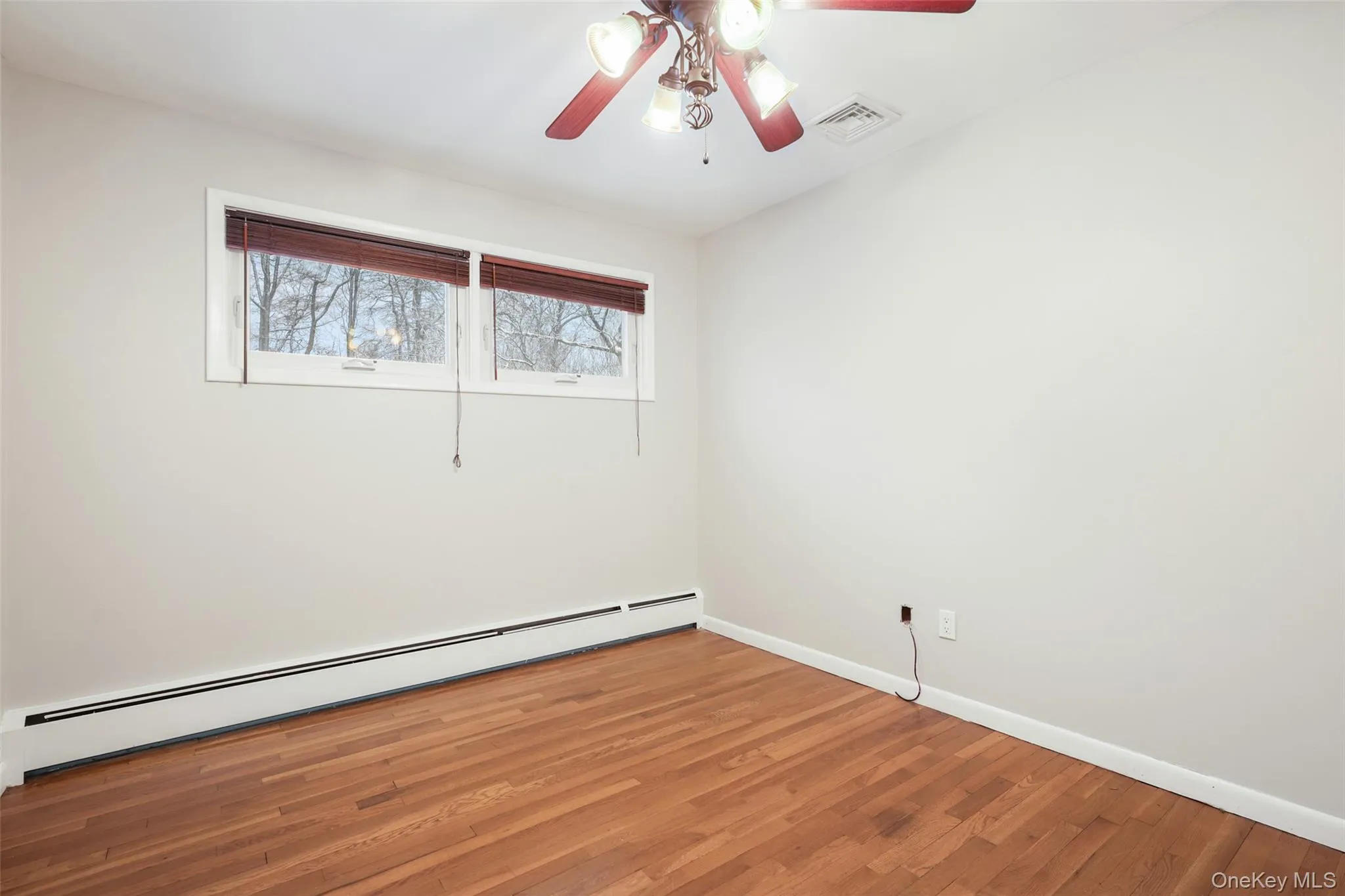 Unfurnished room with baseboard heating, light wood-style flooring, and a ceiling fan Unfurnished room with baseboard heating, light wood-style flooring, and a ceiling fan