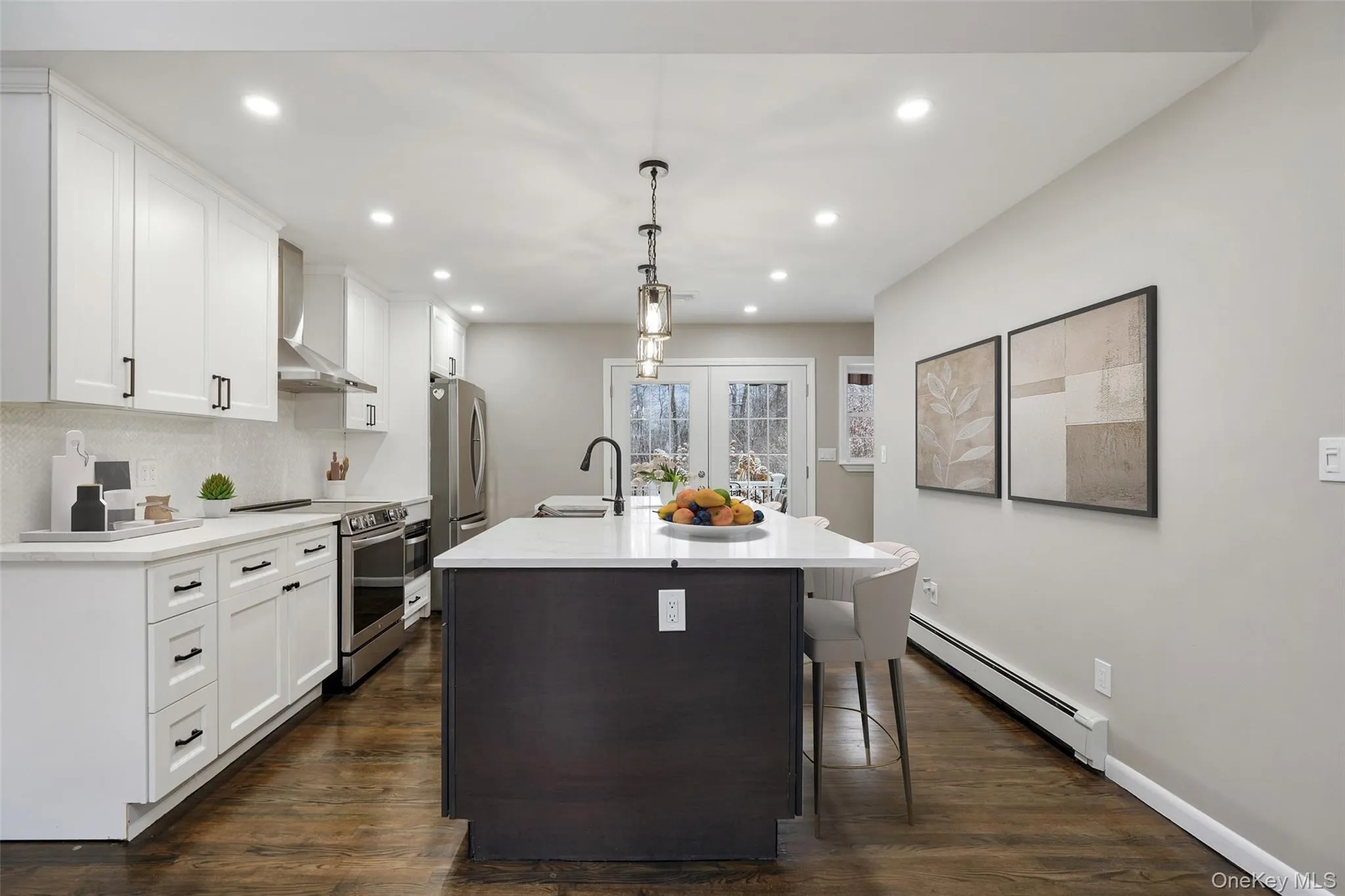 Kitchen with a baseboard radiator, stainless steel appliances, two tone cabinetry, a kitchen breakfast bar, and a kitchen island with sink. *Virtually Staged* Kitchen with a baseboard radiator, stainless steel appliances, two tone cabinetry, a kitchen breakfast bar, and a kitchen island with sink. *Virtually Staged*