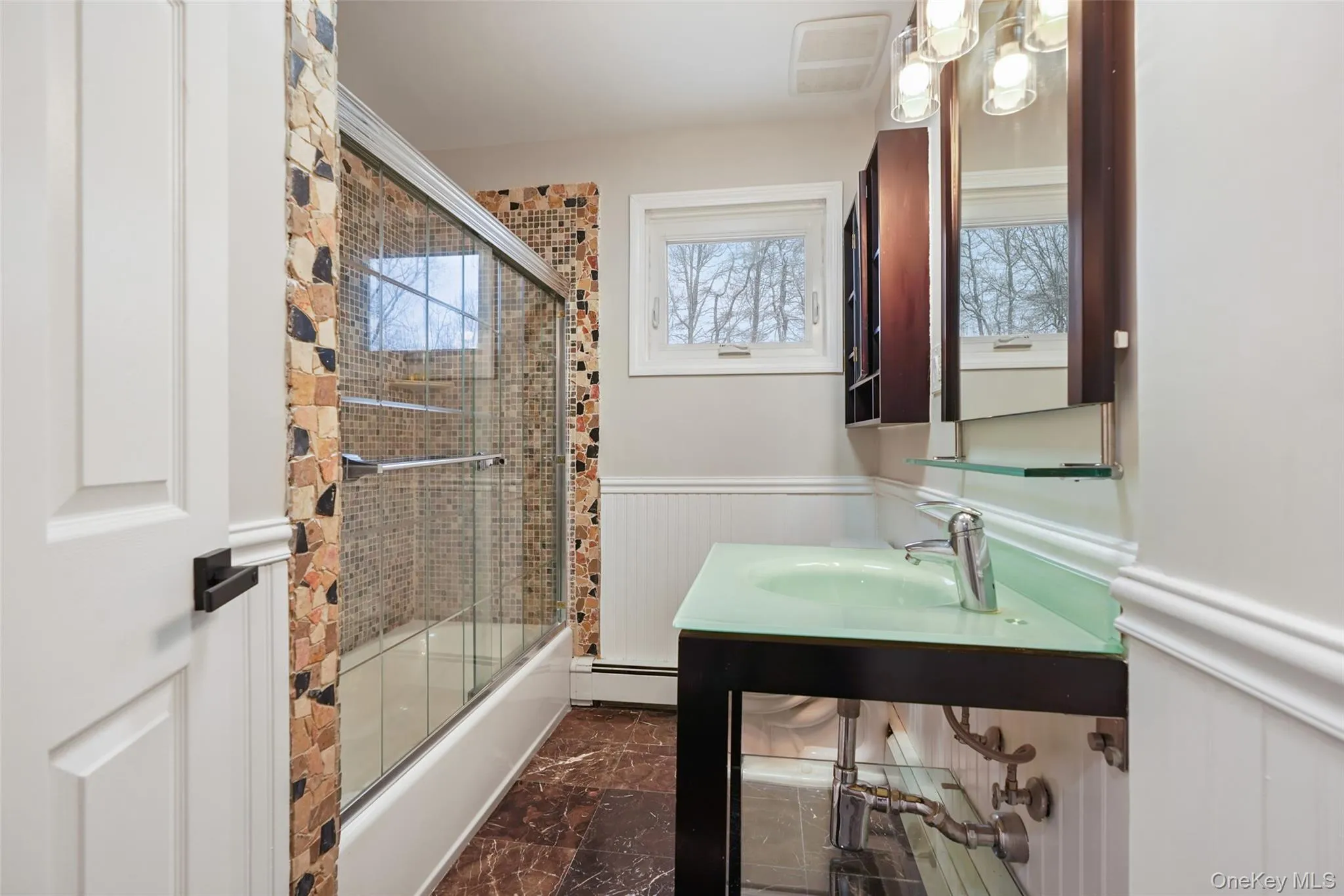 Full bath featuring a wainscoted wall, bath / shower combo with glass door, and a baseboard radiator Full bath featuring a wainscoted wall, bath / shower combo with glass door, and a baseboard radiator