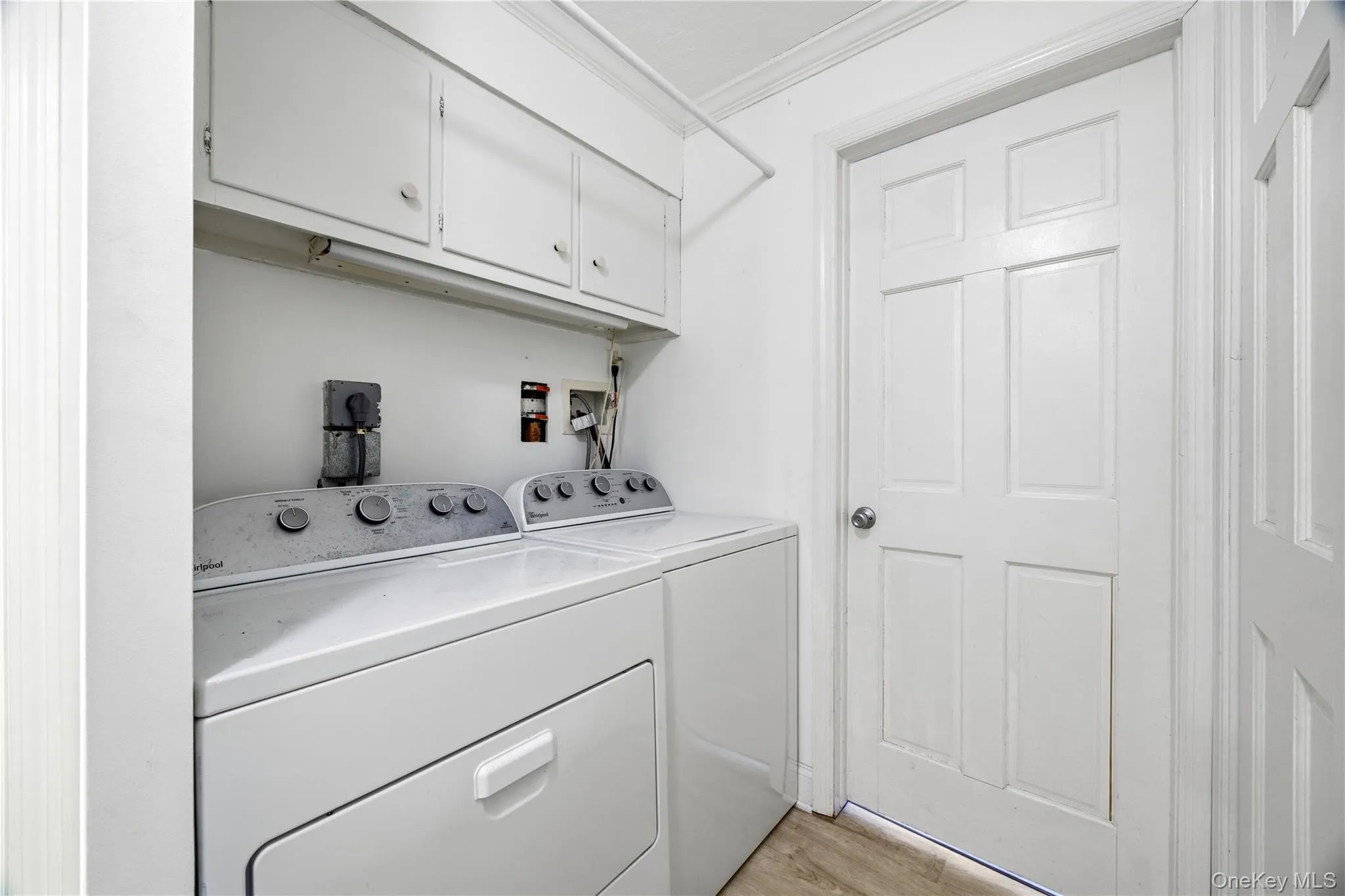 Laundry near bedrooms with ornamental molding, light wood-style floors, washing machine and dryer, and cabinet space Laundry near bedrooms with ornamental molding, light wood-style floors, washing machine and dryer, and cabinet space