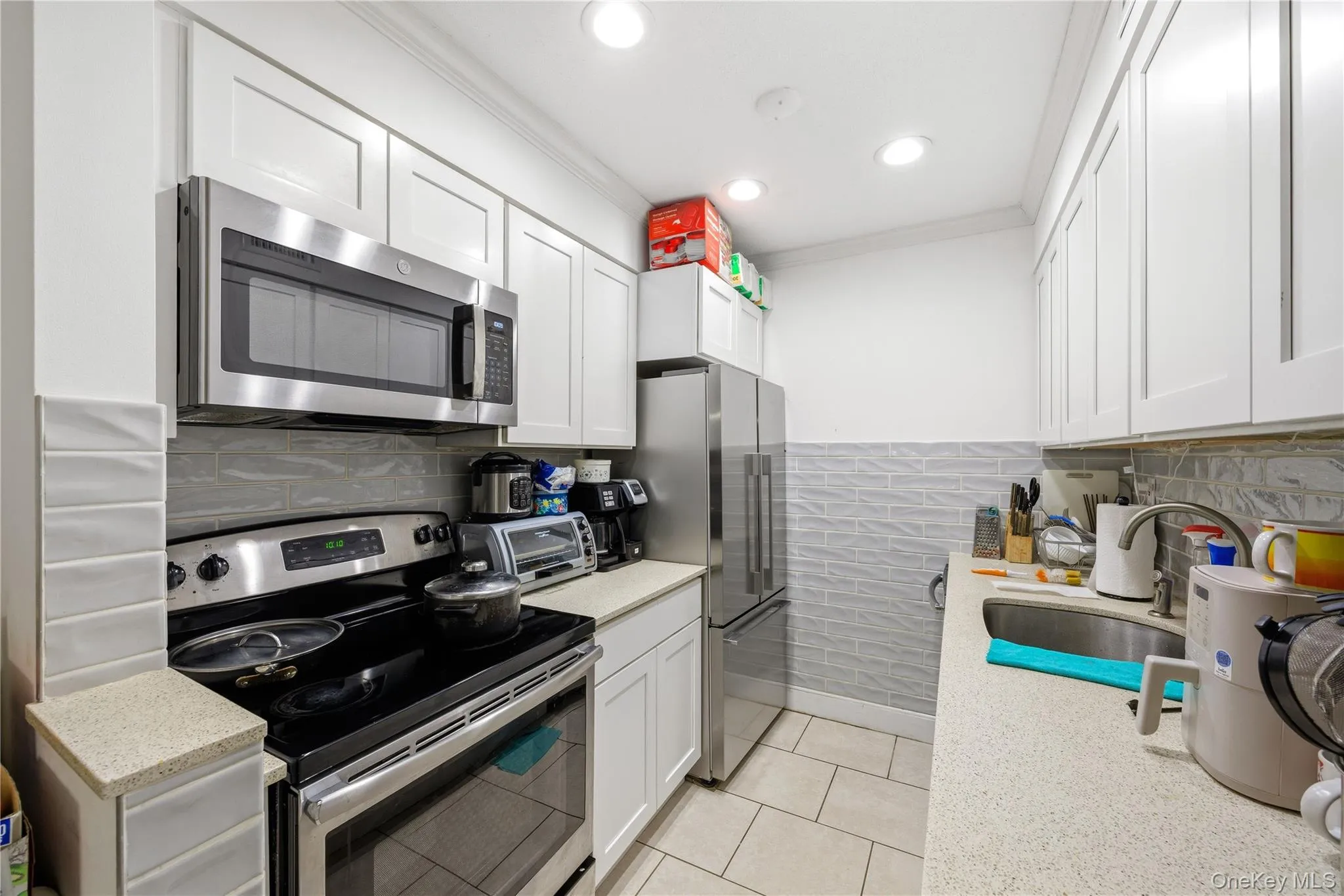 Kitchen with stainless steel appliances, white cabinetry, light stone counters, light tile patterned floors, and tile walls Kitchen with stainless steel appliances, white cabinetry, light stone counters, light tile patterned floors, and tile walls