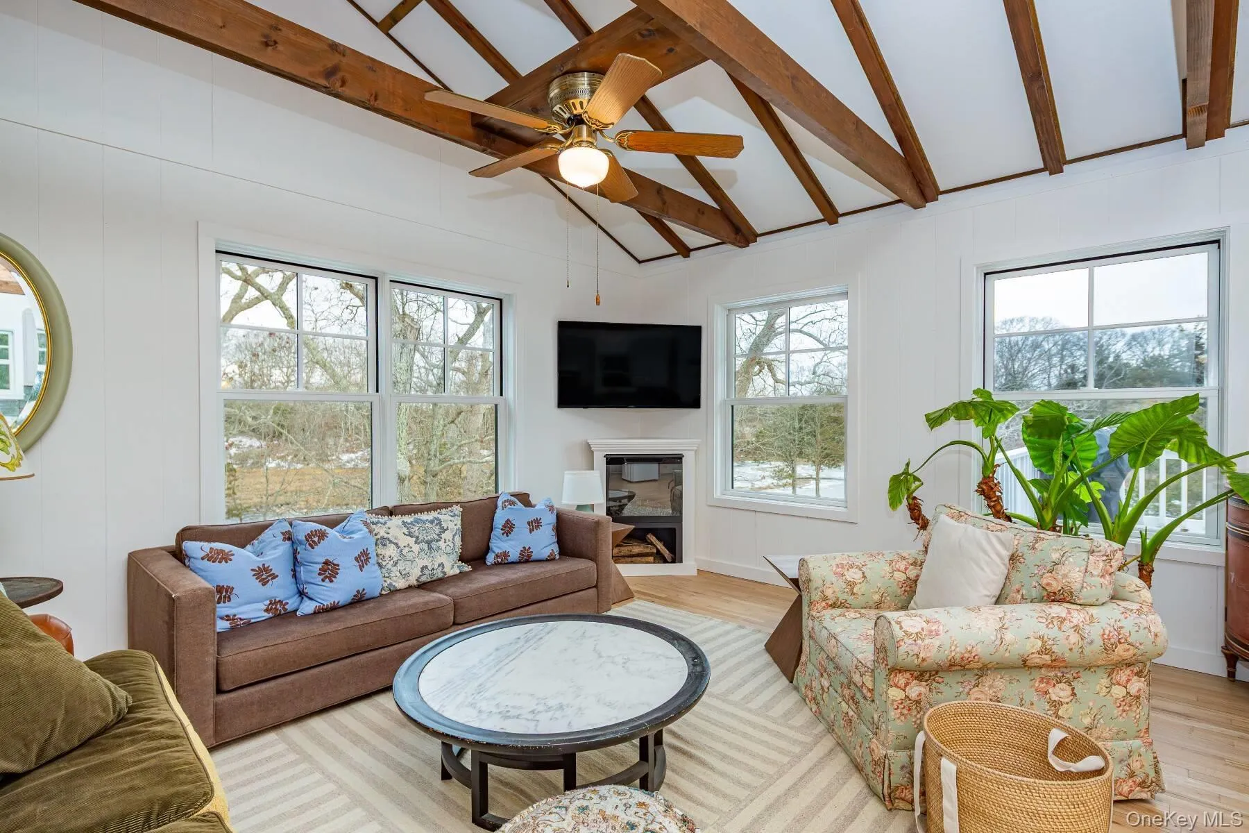 Living room featuring a ceiling fan, lofted ceiling with beams, a fireplace, and light wood-style flooring