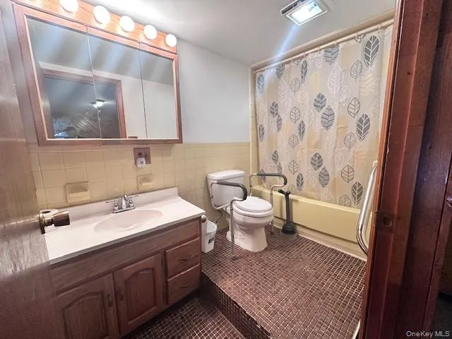 Bathroom featuring tile walls, vanity, shower / tub combo, and dark tile patterned flooring Bathroom featuring tile walls, vanity, shower / tub combo, and dark tile patterned flooring