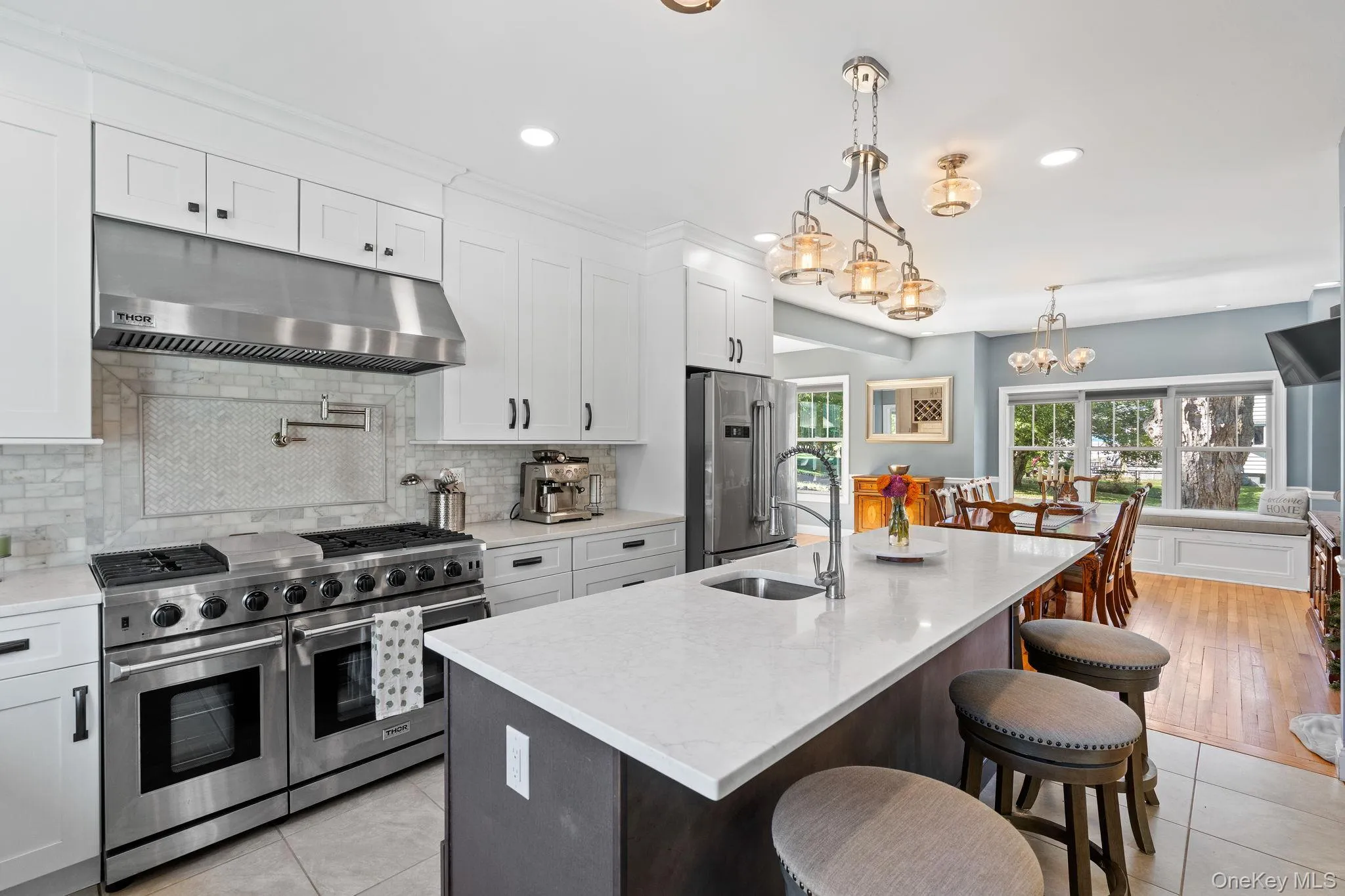 Kitchen featuring high end appliances, under cabinet range hood, white cabinets, a kitchen bar, and light stone counters Kitchen featuring high end appliances, under cabinet range hood, white cabinets, a kitchen bar, and light stone counters