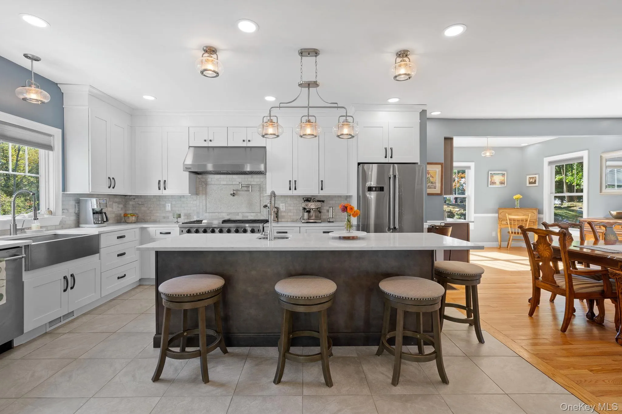 Kitchen with light tile patterned flooring, decorative backsplash, white cabinetry, a kitchen breakfast bar, and an island with sink Kitchen with light tile patterned flooring, decorative backsplash, white cabinetry, a kitchen breakfast bar, and an island with sink