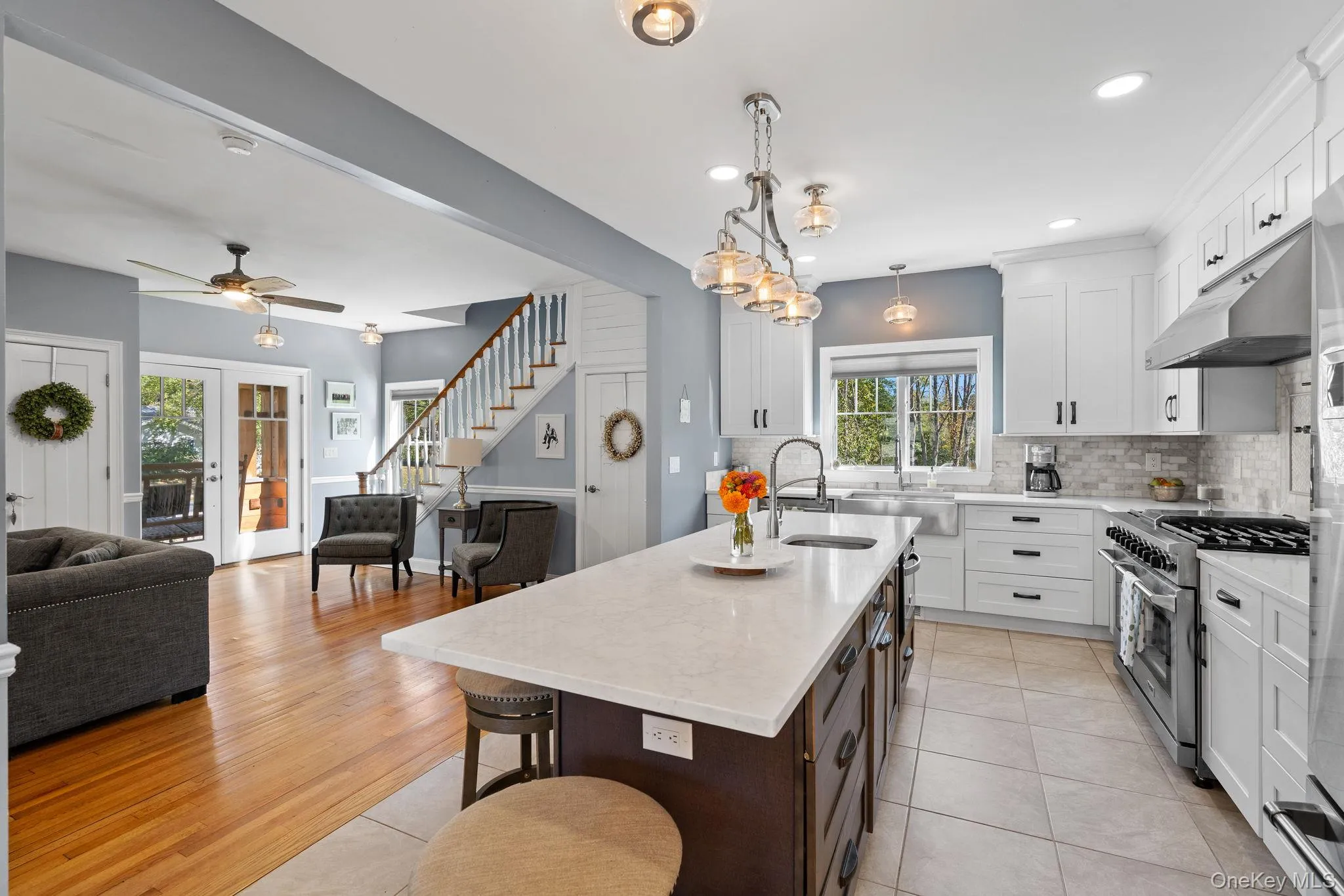 Kitchen with open floor plan, decorative light fixtures, a kitchen island with sink, decorative backsplash, and white cabinets Kitchen with open floor plan, decorative light fixtures, a kitchen island with sink, decorative backsplash, and white cabinets