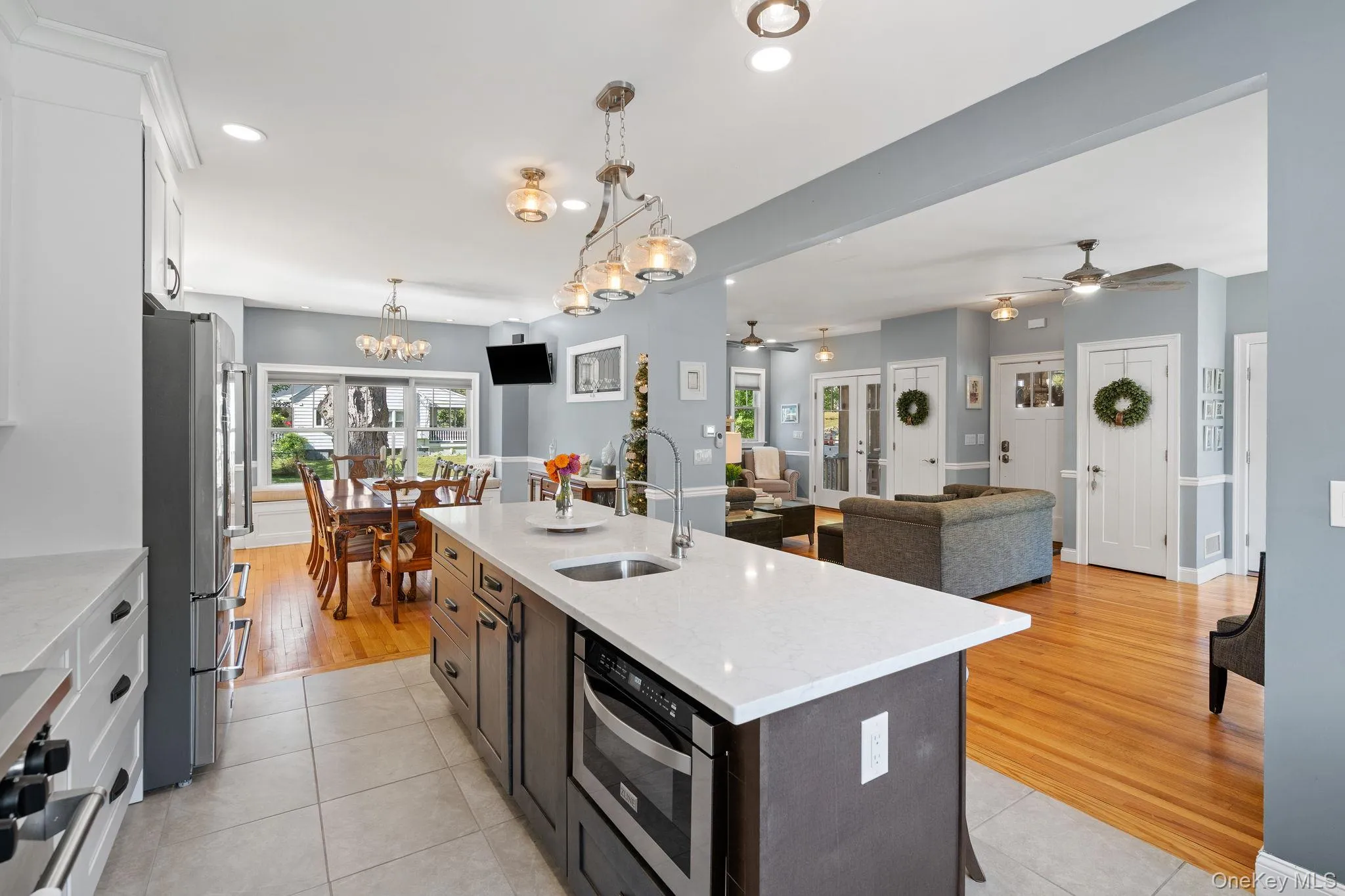 Kitchen with white cabinets, decorative light fixtures, a kitchen island with sink, open floor plan, and light stone countertops Kitchen with white cabinets, decorative light fixtures, a kitchen island with sink, open floor plan, and light stone countertops