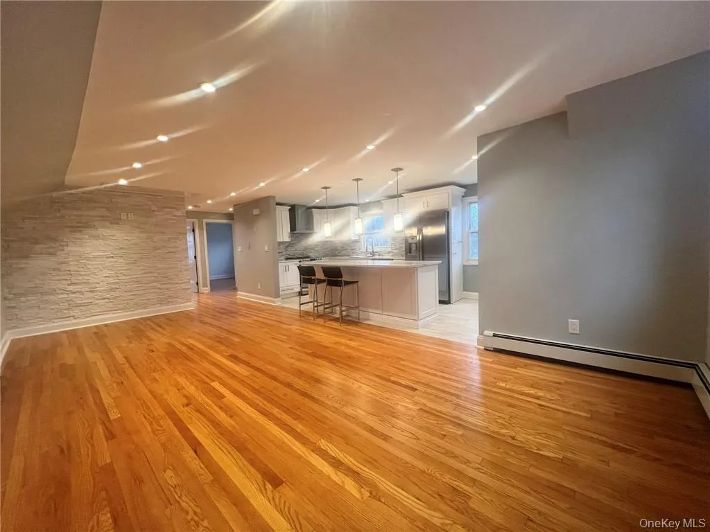 Unfurnished living room featuring light wood-type flooring and baseboard heating Unfurnished living room featuring light wood-type flooring and baseboard heating