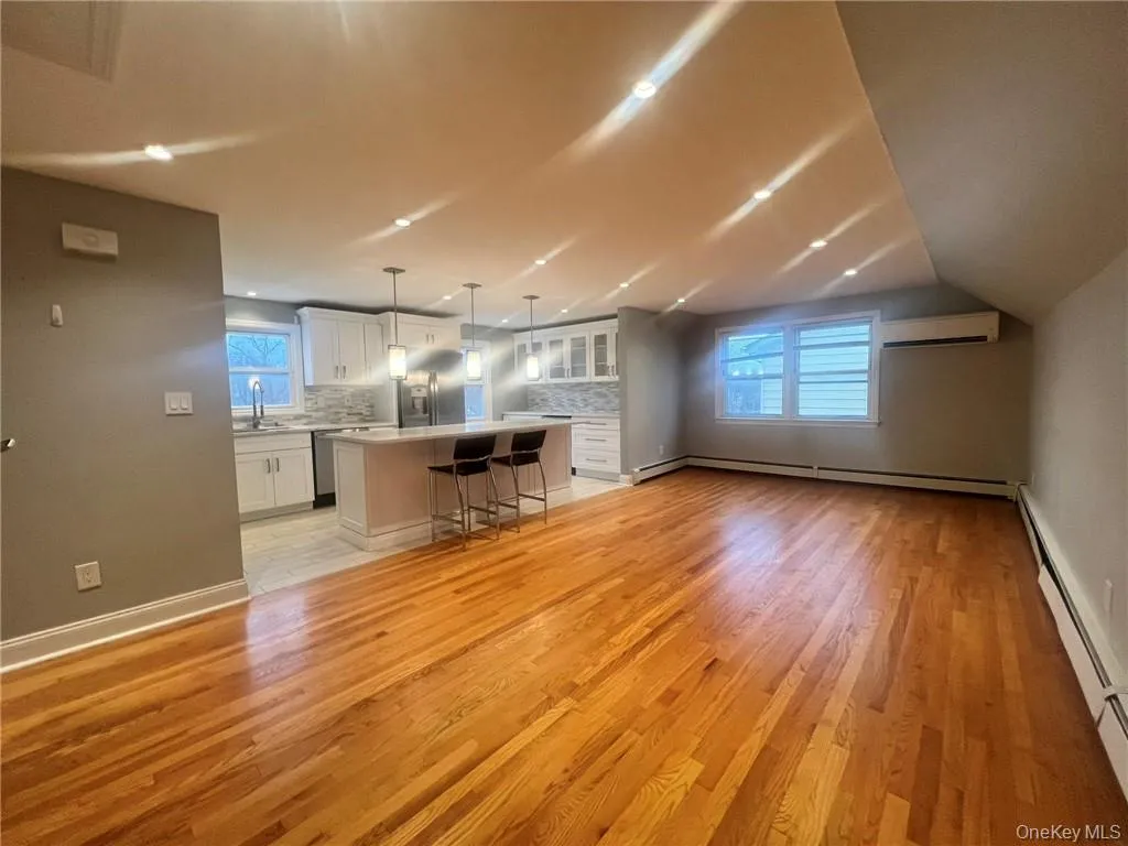 Kitchen with white cabinets, a breakfast bar, light wood-style floors, light countertops, and glass insert cabinets Kitchen with white cabinets, a breakfast bar, light wood-style floors, light countertops, and glass insert cabinets