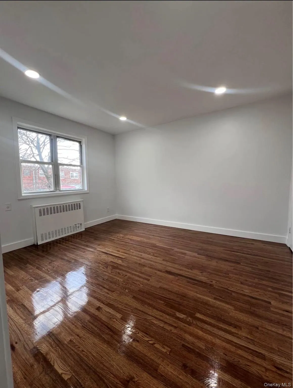 Empty room with dark wood finished floors, radiator, and recessed lighting Empty room with dark wood finished floors, radiator, and recessed lighting