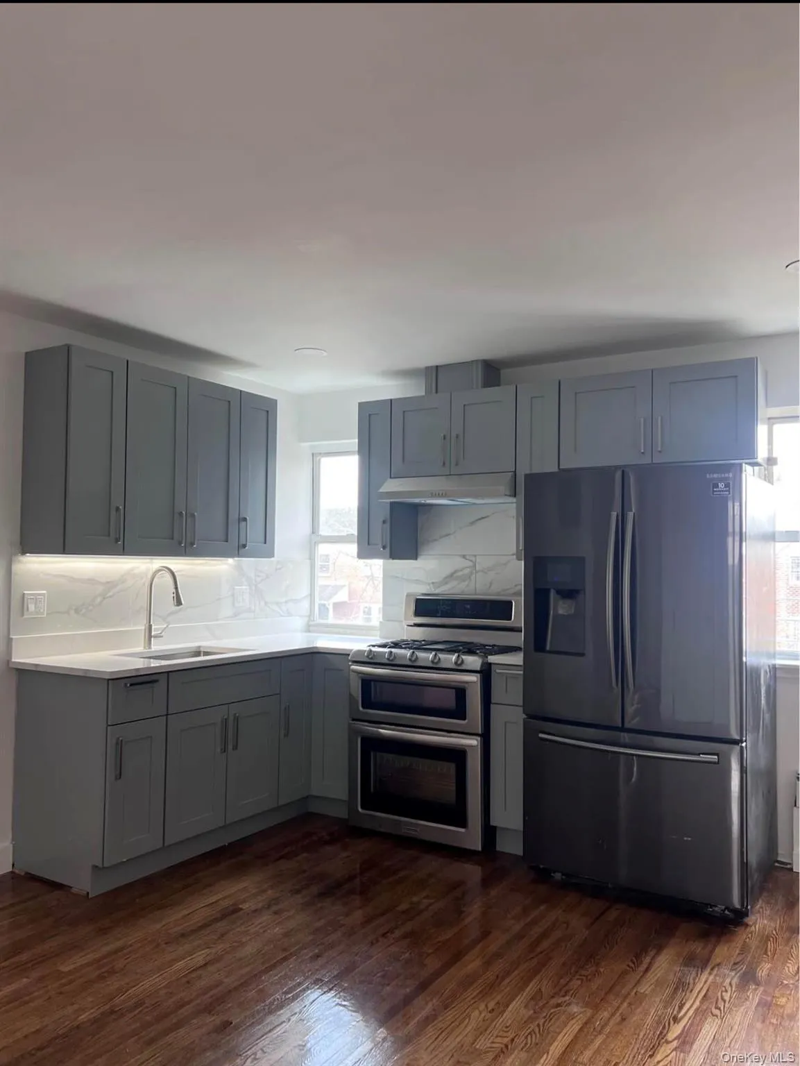 Kitchen featuring stainless steel appliances, gray cabinetry, dark wood-type flooring, tasteful backsplash, and light stone countertops Kitchen featuring stainless steel appliances, gray cabinetry, dark wood-type flooring, tasteful backsplash, and light stone countertops