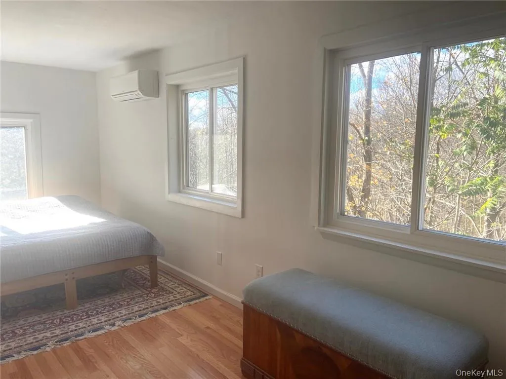 Bedroom featuring hardwood / wood-style floors, a wall unit AC, and multiple windows Bedroom featuring hardwood / wood-style floors, a wall unit AC, and multiple windows