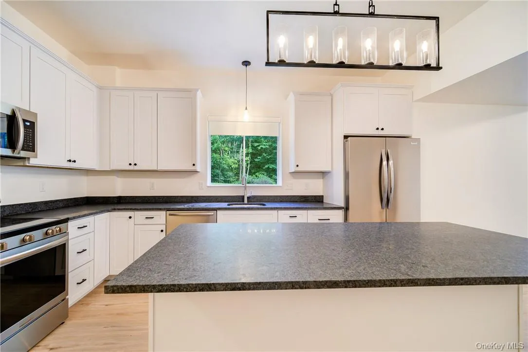 Kitchen featuring appliances with stainless steel finishes, decorative light fixtures, white cabinets, and light hardwood / wood-style flooring Kitchen featuring appliances with stainless steel finishes, decorative light fixtures, white cabinets, and light hardwood / wood-style flooring