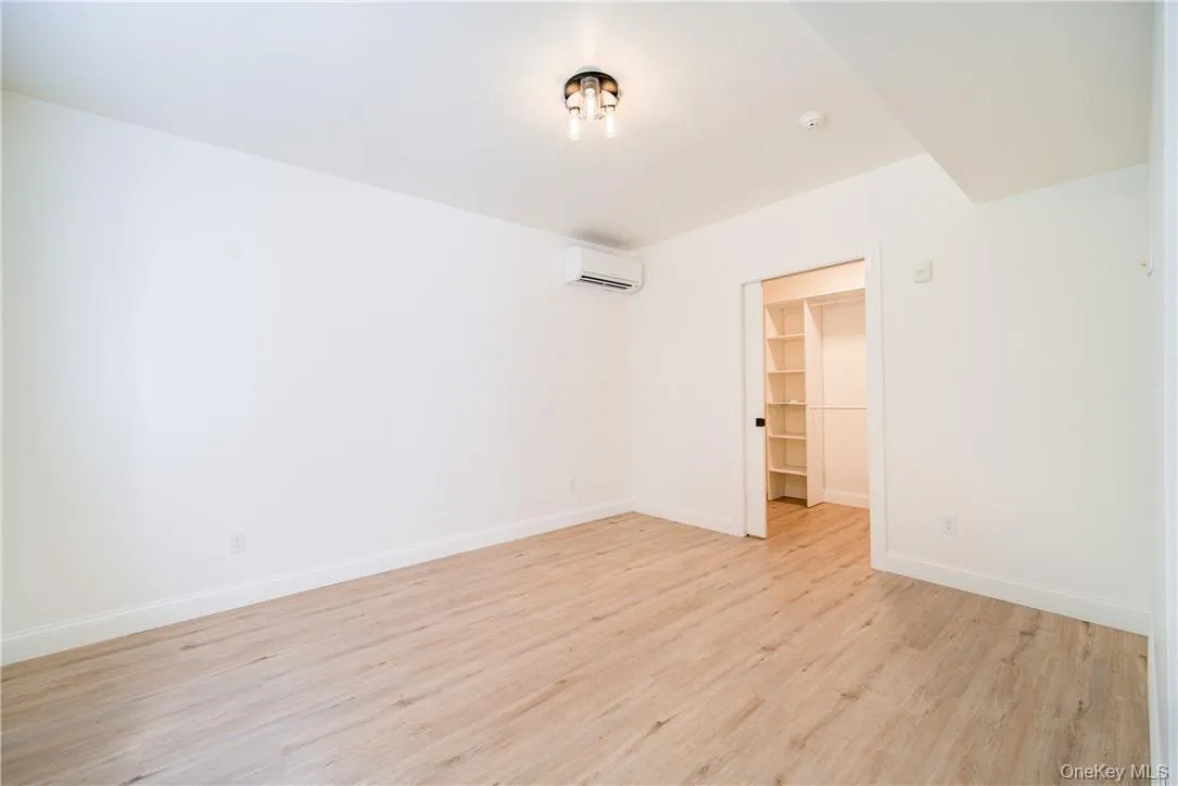 Unfurnished bedroom featuring an AC wall unit, a closet, light hardwood / wood-style floors, and a walk in closet Unfurnished bedroom featuring an AC wall unit, a closet, light hardwood / wood-style floors, and a walk in closet