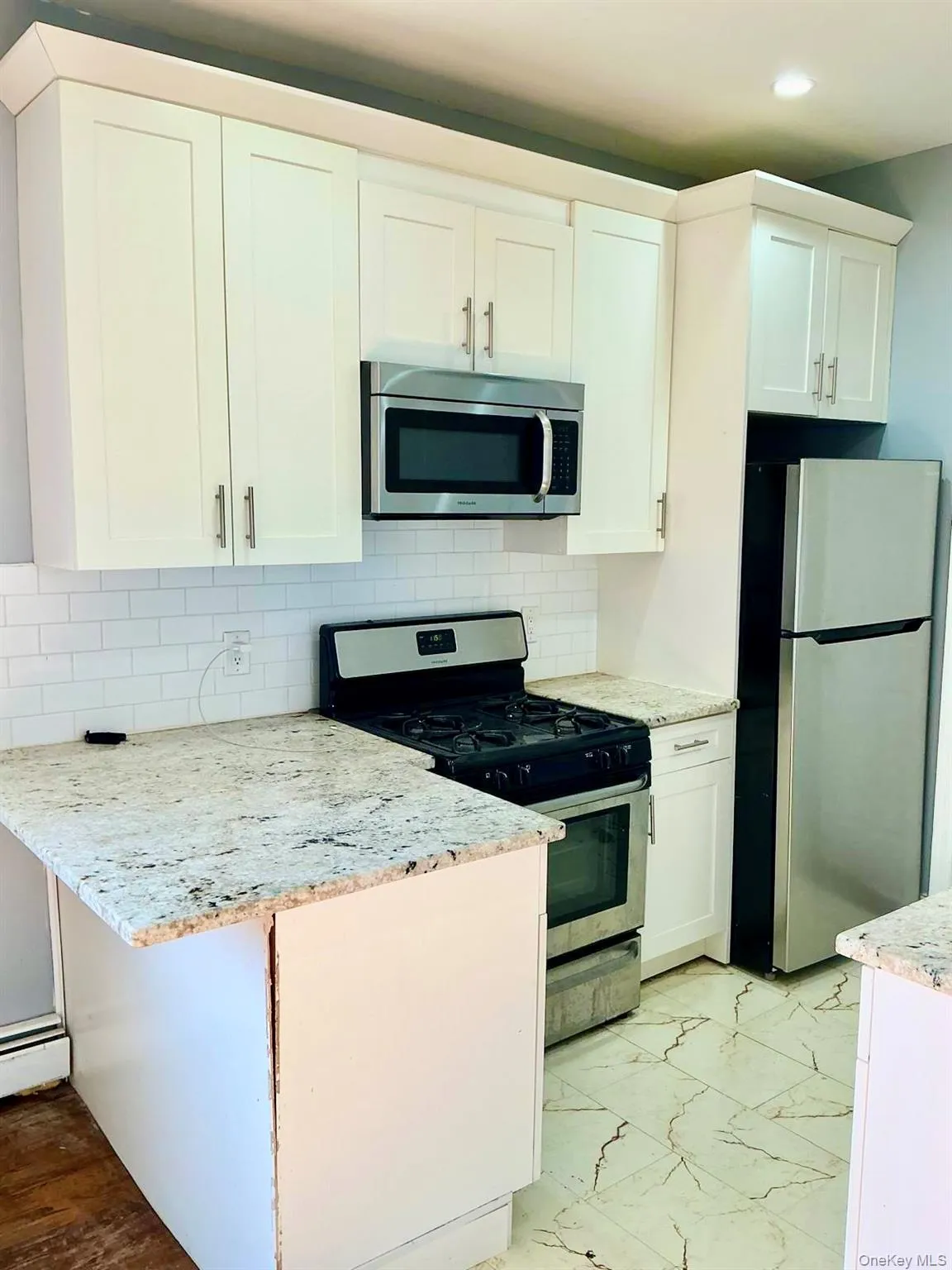 Kitchen featuring stainless steel appliances, white cabinets, light stone countertops, backsplash, and light marble finish floors Kitchen featuring stainless steel appliances, white cabinets, light stone countertops, backsplash, and light marble finish floors