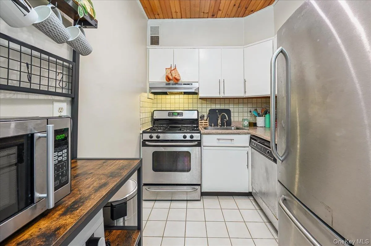 Kitchen featuring stainless steel appliances, light tile patterned floors, white cabinetry, wood ceiling, and tasteful backsplash Kitchen featuring stainless steel appliances, light tile patterned floors, white cabinetry, wood ceiling, and tasteful backsplash