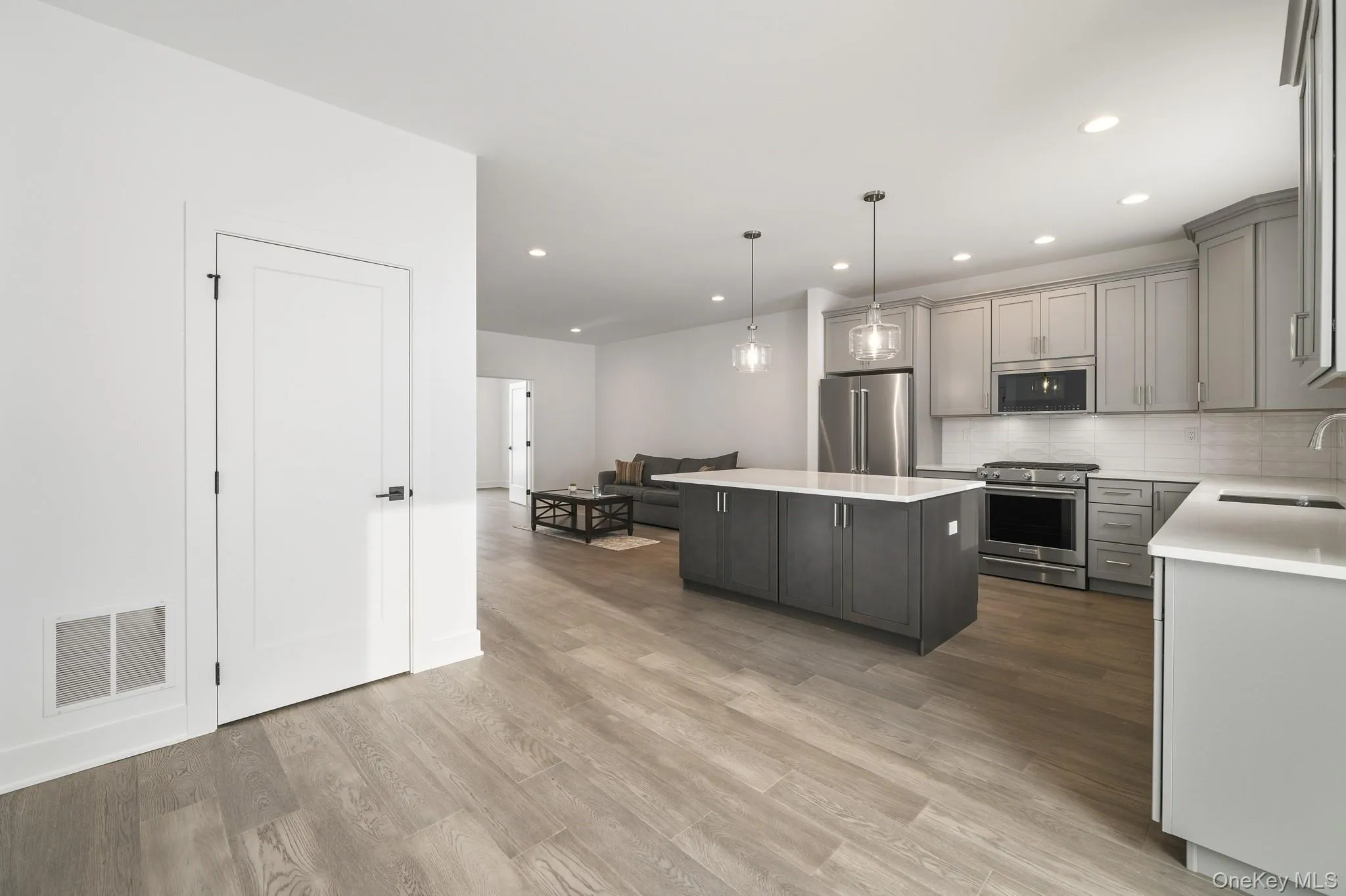 Kitchen with gray cabinets, appliances with stainless steel finishes, pendant lighting, a kitchen island, and backsplash Kitchen with gray cabinets, appliances with stainless steel finishes, pendant lighting, a kitchen island, and backsplash