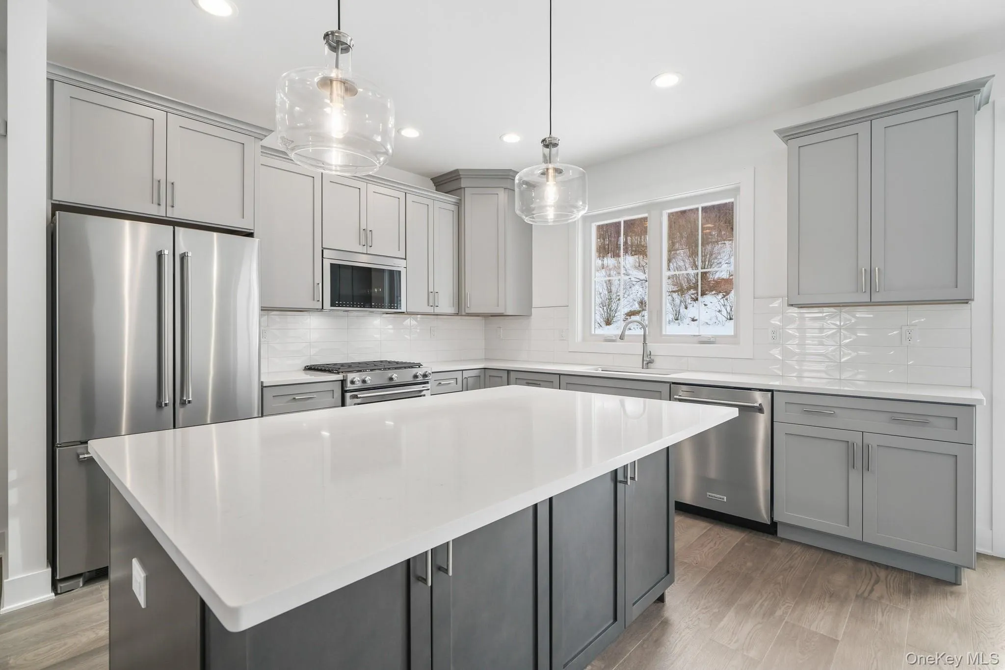 Kitchen with gray cabinets, premium appliances, decorative light fixtures, light wood-style floors, and recessed lighting Kitchen with gray cabinets, premium appliances, decorative light fixtures, light wood-style floors, and recessed lighting