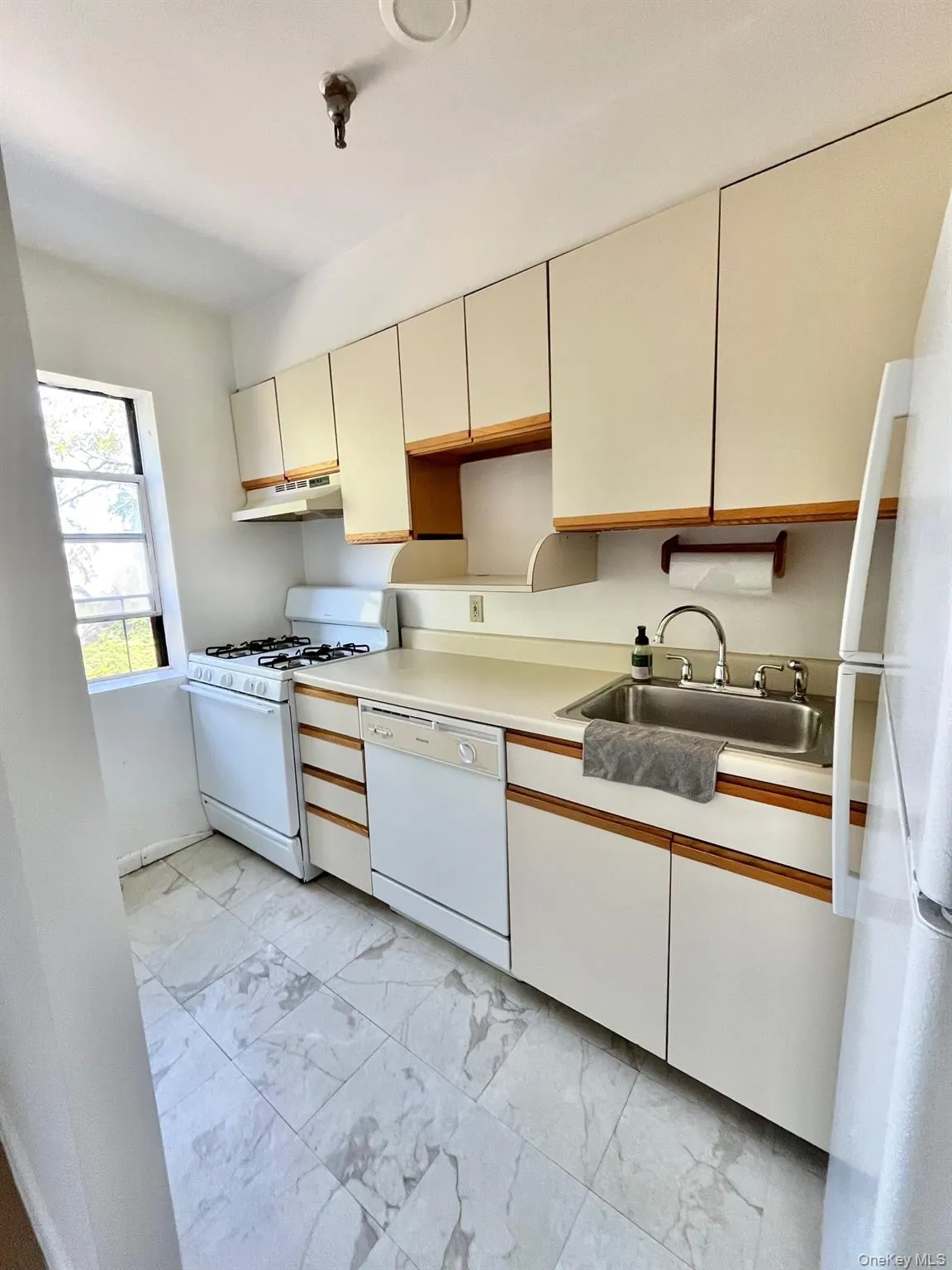 Kitchen with white appliances, light marble finish floors, light countertops, cream cabinetry, and under cabinet range hood Kitchen with white appliances, light marble finish floors, light countertops, cream cabinetry, and under cabinet range hood