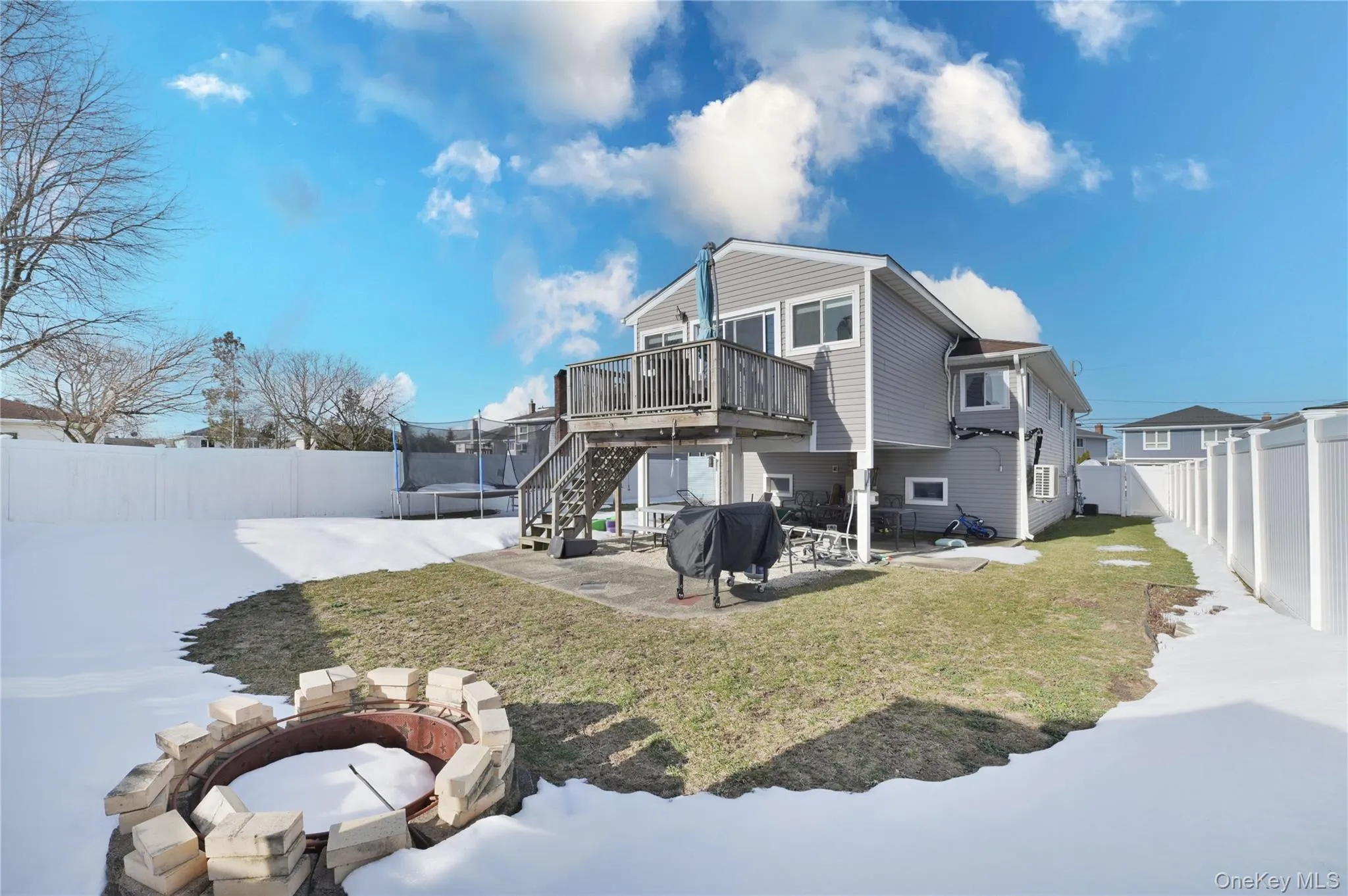 Rear view of property featuring a patio, a fire pit, a fenced backyard, a wooden deck, and a trampoline Rear view of property featuring a patio, a fire pit, a fenced backyard, a wooden deck, and a trampoline