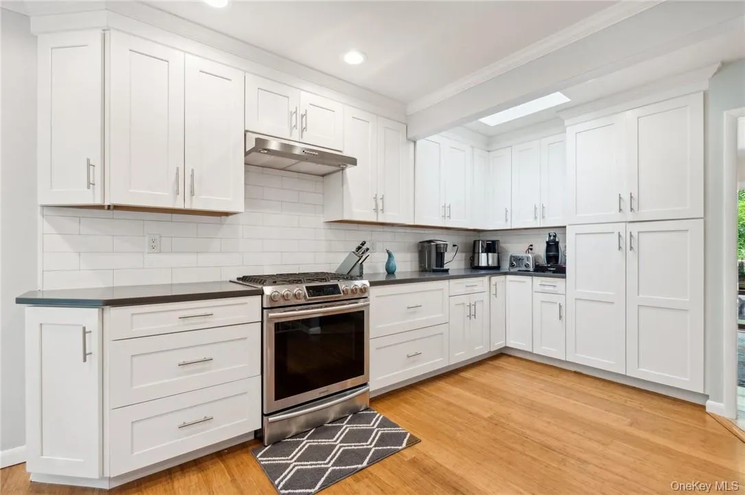 Kitchen with light hardwood / wood-style flooring, crown molding, stainless steel range with gas stovetop, backsplash, and white cabinetry Kitchen with light hardwood / wood-style flooring, crown molding, stainless steel range with gas stovetop, backsplash, and white cabinetry