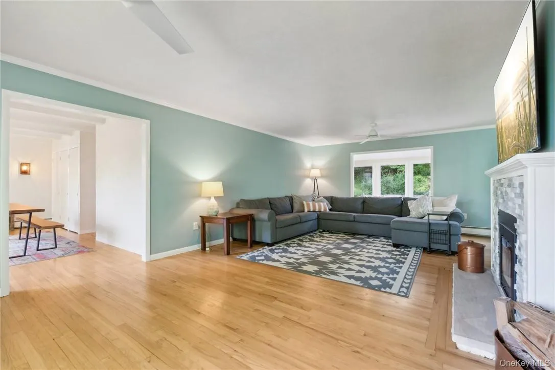 Living room with a baseboard heating unit, ceiling fan, light wood-type flooring, and crown molding Living room with a baseboard heating unit, ceiling fan, light wood-type flooring, and crown molding