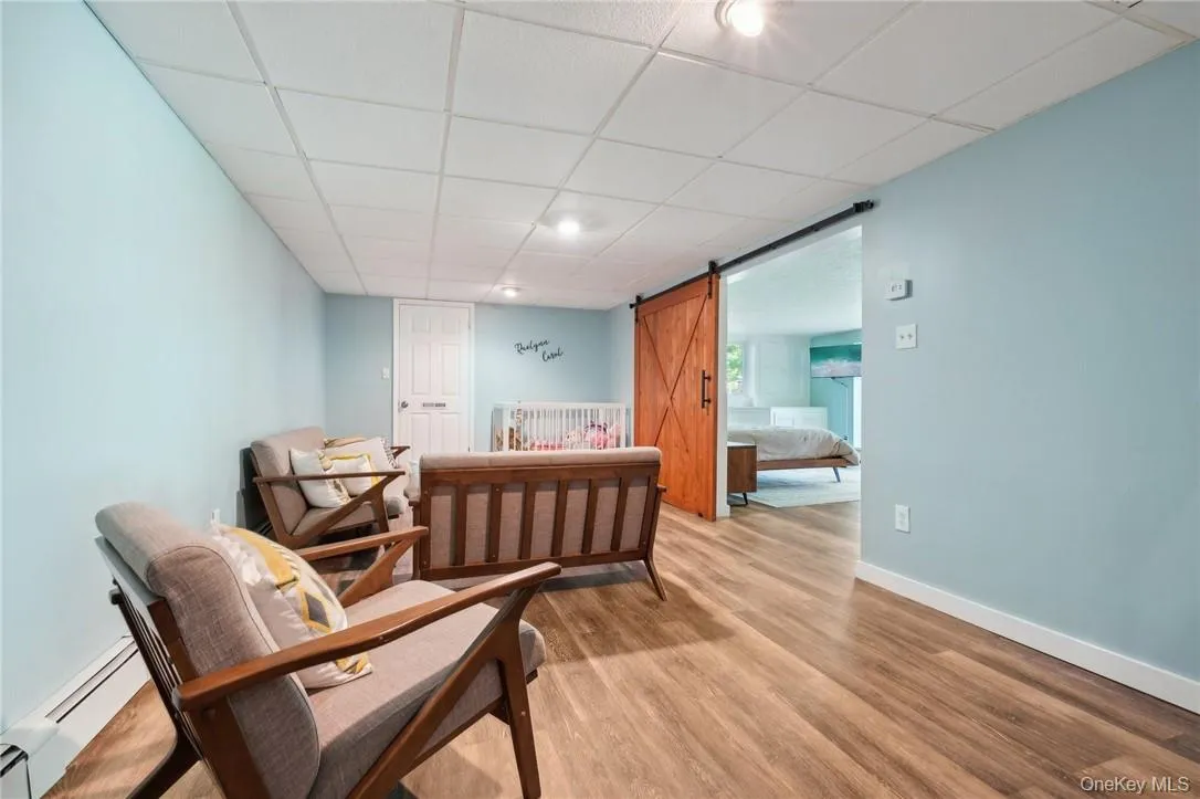 Sitting room featuring baseboard heating, a barn door, hardwood / wood-style flooring, and a drop ceiling Sitting room featuring baseboard heating, a barn door, hardwood / wood-style flooring, and a drop ceiling