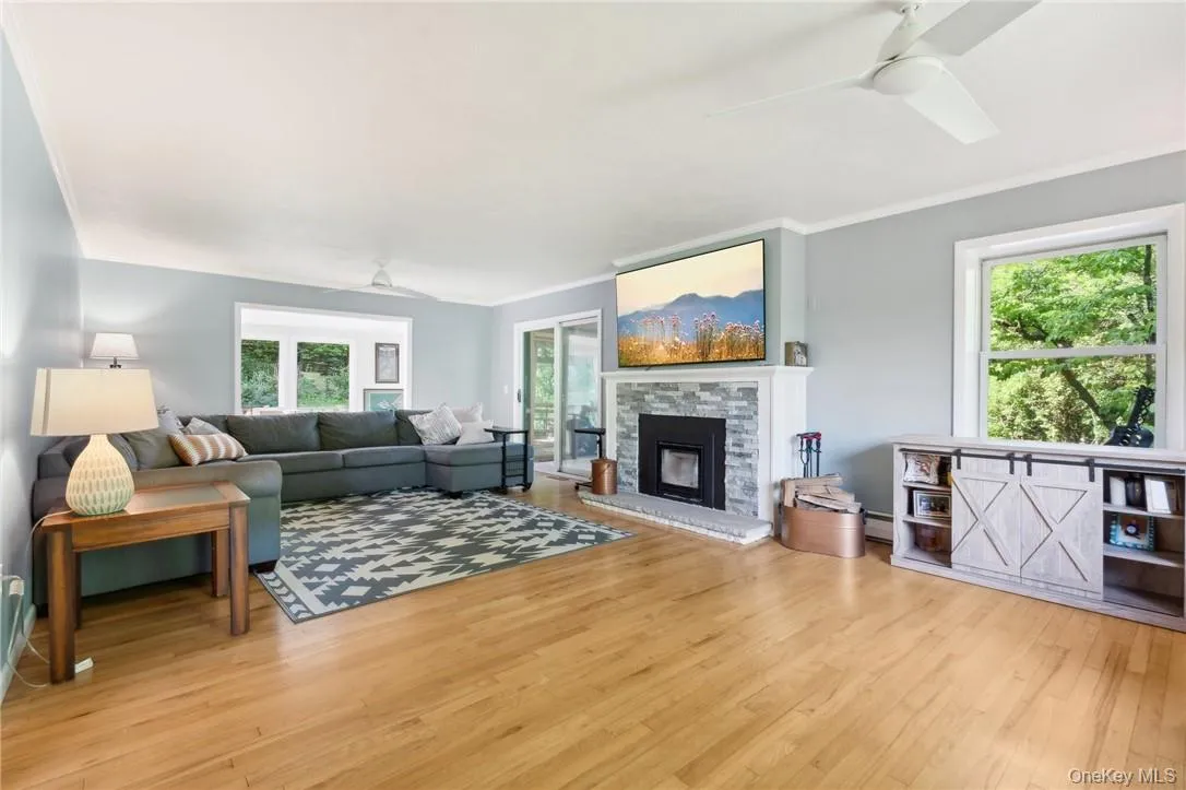 Living room with a stone fireplace, light hardwood / wood-style floors, crown molding, and ceiling fan Living room with a stone fireplace, light hardwood / wood-style floors, crown molding, and ceiling fan