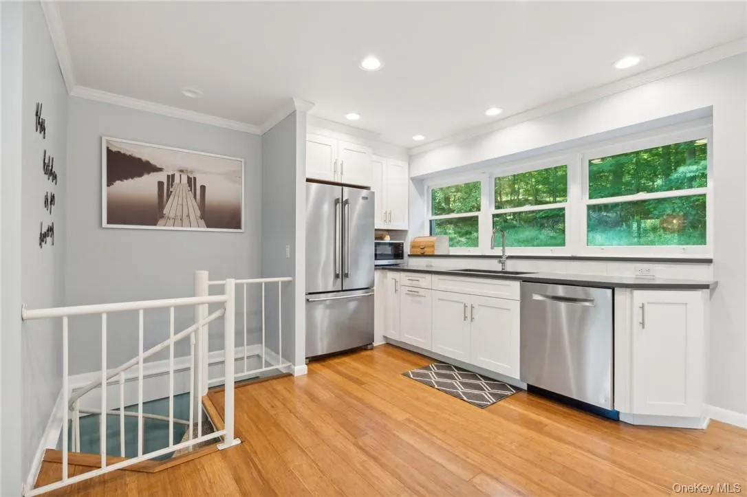 Kitchen featuring light hardwood / wood-style floors, crown molding, stainless steel appliances, white cabinets, and sink Kitchen featuring light hardwood / wood-style floors, crown molding, stainless steel appliances, white cabinets, and sink