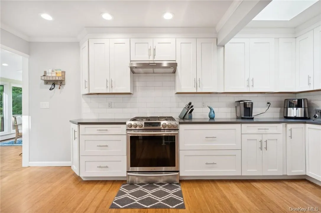 Kitchen featuring stainless steel range with gas stovetop, white cabinets, tasteful backsplash, and light hardwood / wood-style flooring Kitchen featuring stainless steel range with gas stovetop, white cabinets, tasteful backsplash, and light hardwood / wood-style flooring