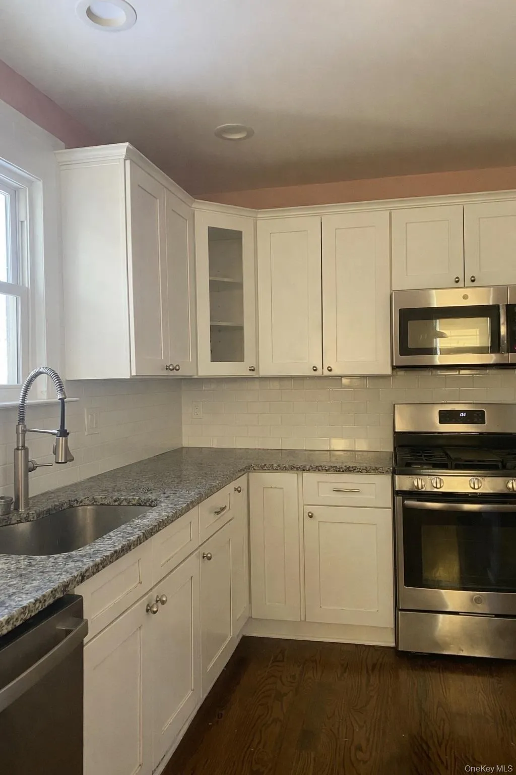 Kitchen featuring stainless steel appliances, white cabinets, glass insert cabinets, and dark stone counters Kitchen featuring stainless steel appliances, white cabinets, glass insert cabinets, and dark stone counters