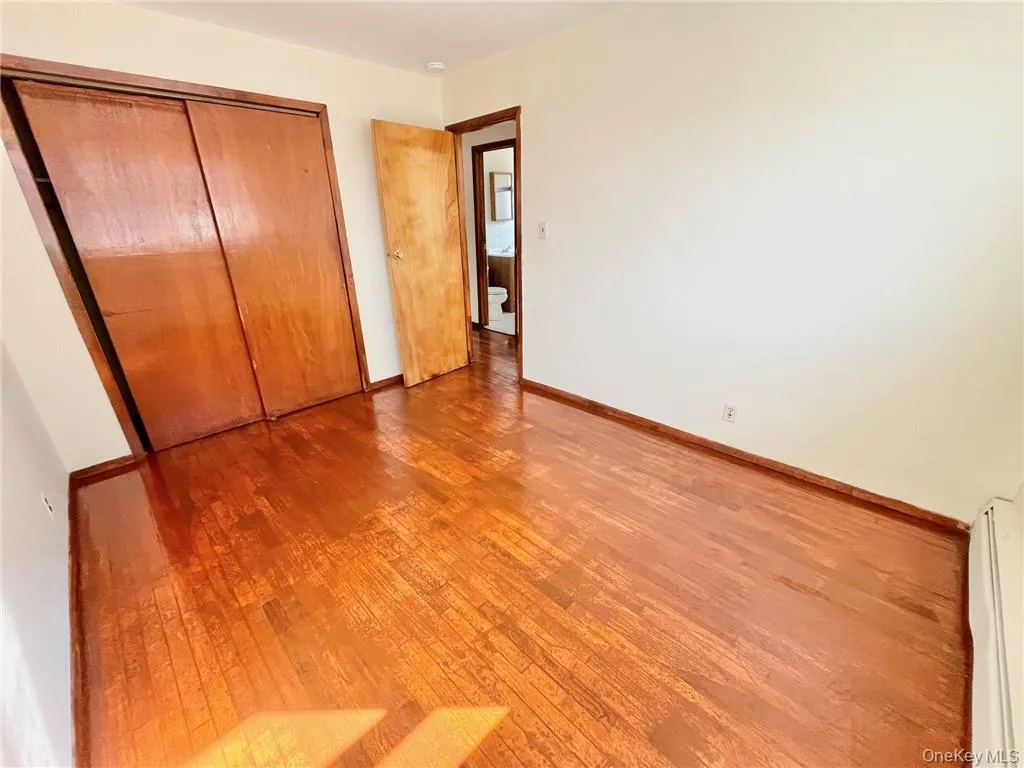 Unfurnished bedroom with baseboard heating, wood-type flooring, and a closet Unfurnished bedroom with baseboard heating, wood-type flooring, and a closet