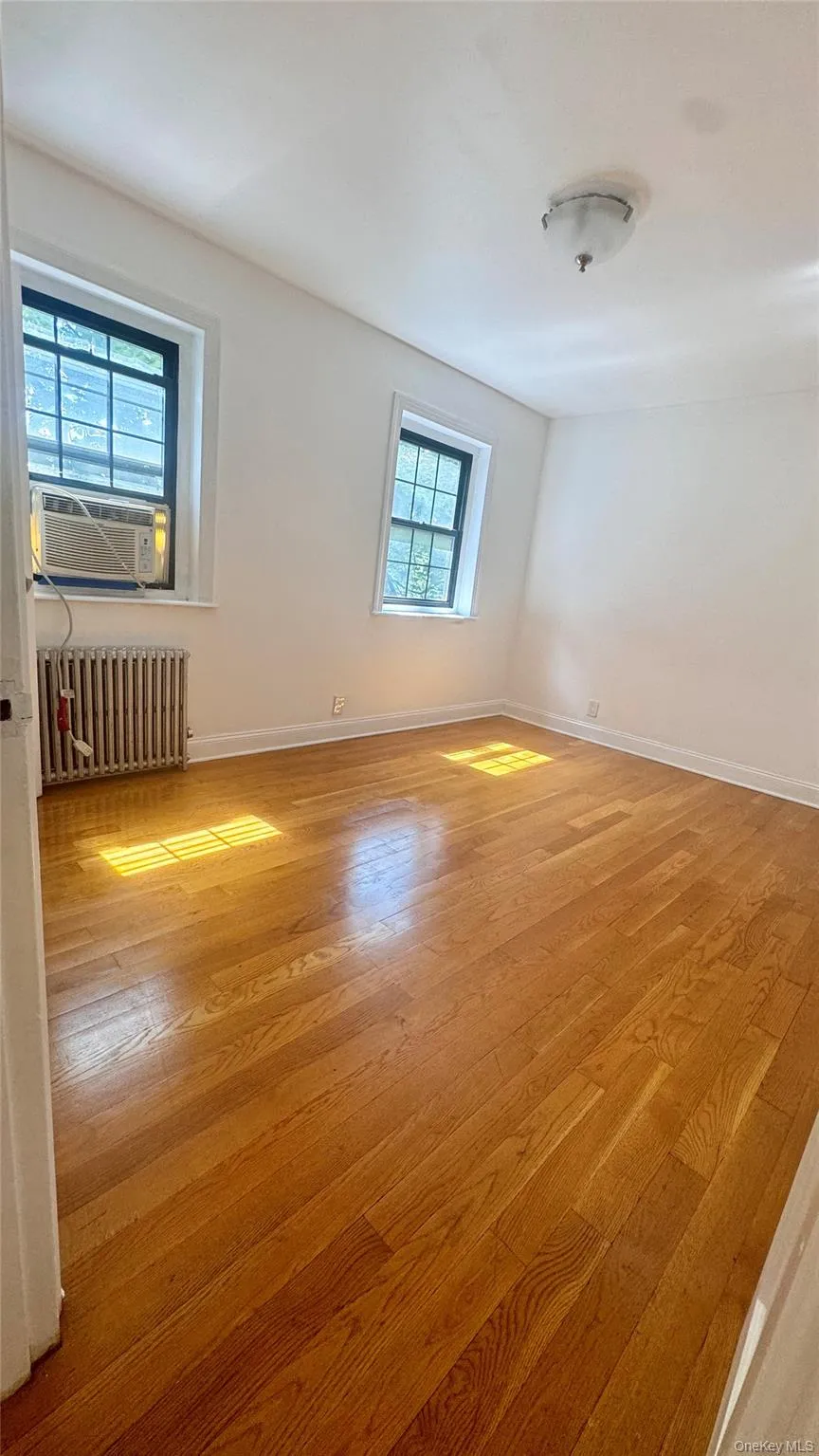 Spare room featuring radiator heating unit, cooling unit, and wood finished floors Spare room featuring radiator heating unit, cooling unit, and wood finished floors