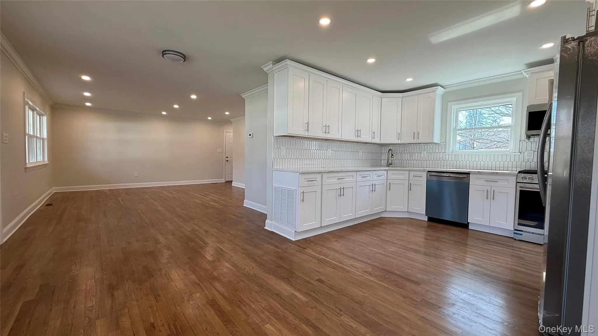 Kitchen featuring white cabinets, stainless steel appliances, ornamental molding, wood finished floors, and tile backsplash with eat-in-kitchen leading to living room Kitchen featuring white cabinets, stainless steel appliances, ornamental molding, wood finished floors, and tile backsplash with eat-in-kitchen leading to living room