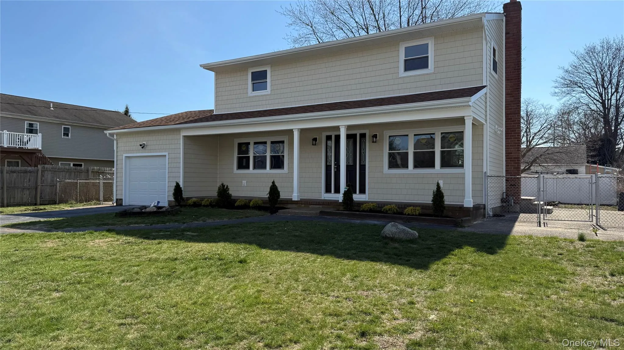 Front facade with a covered porch, an attached one car garage, chimney, asphalt driveway, and chain link fence Front facade with a covered porch, an attached one car garage, chimney, asphalt driveway, and chain link fence