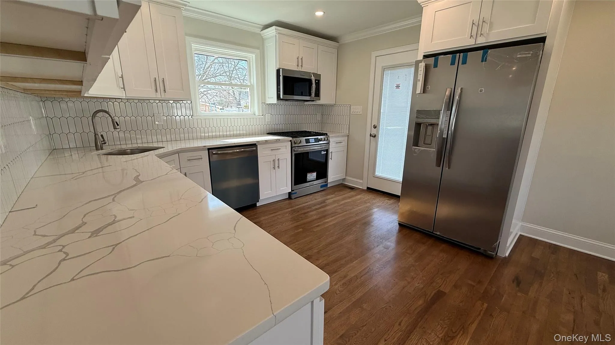 Kitchen featuring white cabinets, stainless steel appliances, ornamental molding, wood finished floors, and tile backsplash Kitchen featuring white cabinets, stainless steel appliances, ornamental molding, wood finished floors, and tile backsplash