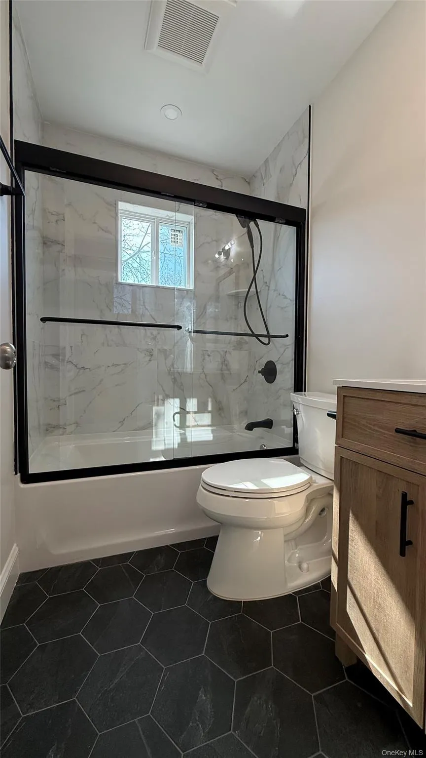 Full bathroom on second floor featuring shower / bath combination with glass door, vanity, and dark tile patterned flooring Full bathroom on second floor featuring shower / bath combination with glass door, vanity, and dark tile patterned flooring