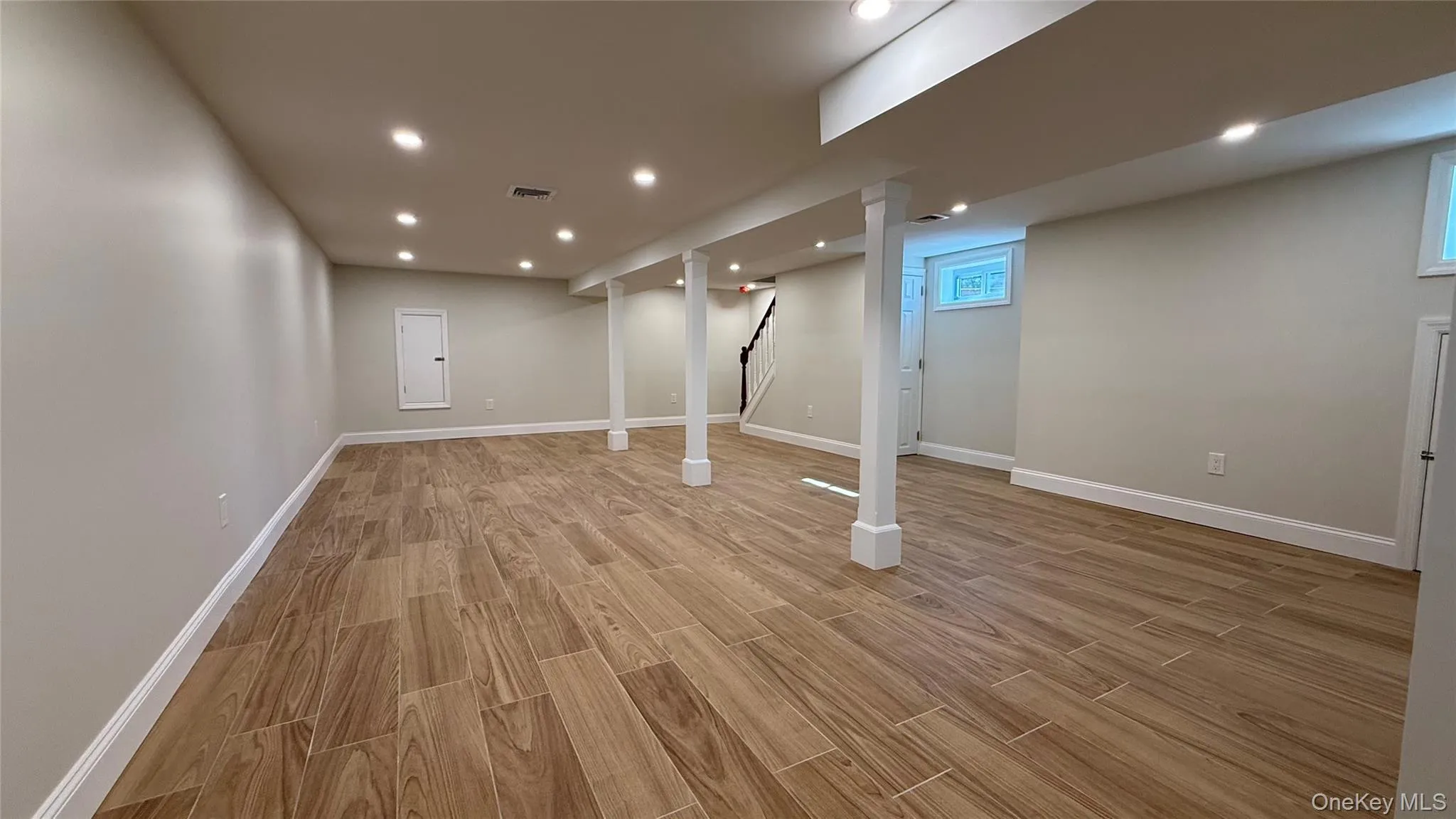 Spacious basement featuring wood-look tile flooring, recessed lighting, support columns, and light-toned walls Spacious basement featuring wood-look tile flooring, recessed lighting, support columns, and light-toned walls