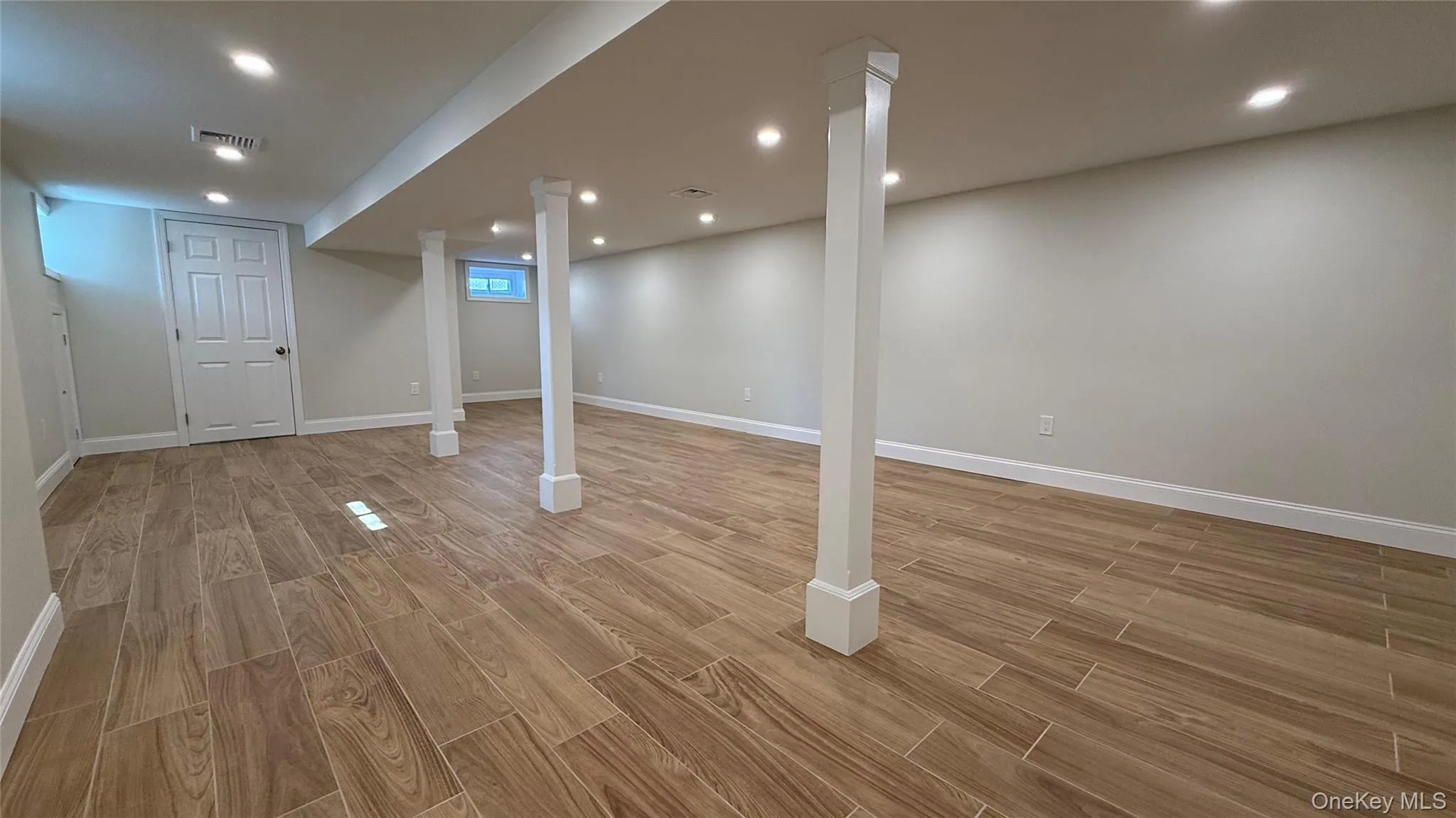 Spacious basement featuring wood-look tile flooring, recessed lighting, support columns, and light-toned walls Spacious basement featuring wood-look tile flooring, recessed lighting, support columns, and light-toned walls