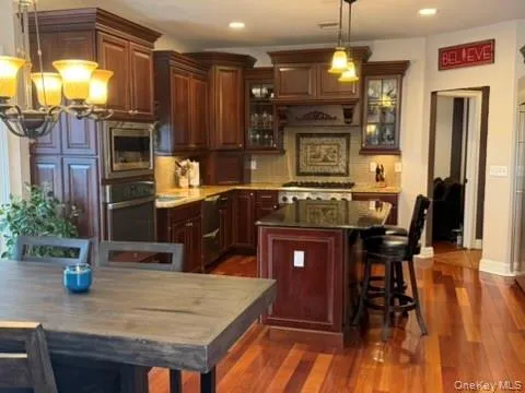 Kitchen featuring a breakfast bar area, a center island, dark wood finished floors, decorative backsplash, and glass fronted cabinets Kitchen featuring a breakfast bar area, a center island, dark wood finished floors, decorative backsplash, and glass fronted cabinets